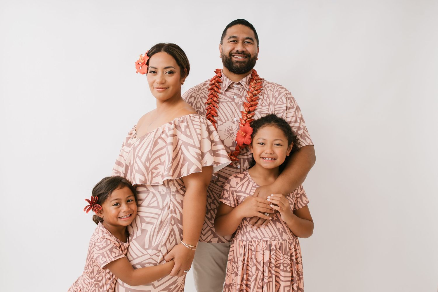 Family in coordinated pink and beige outfits poses together against white background for portrait session.
