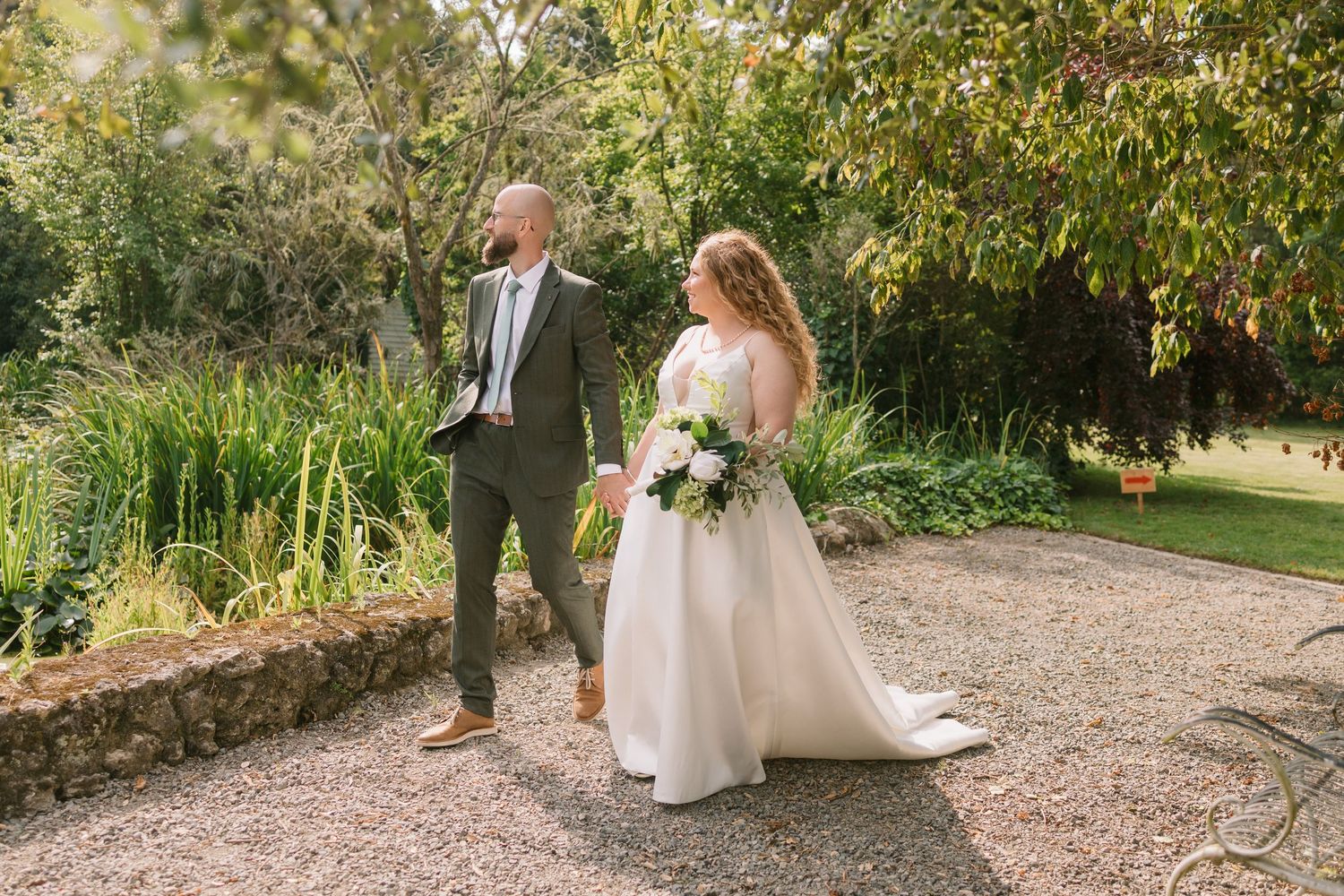 Newlyweds walking together on garden path surrounded by lush greenery.