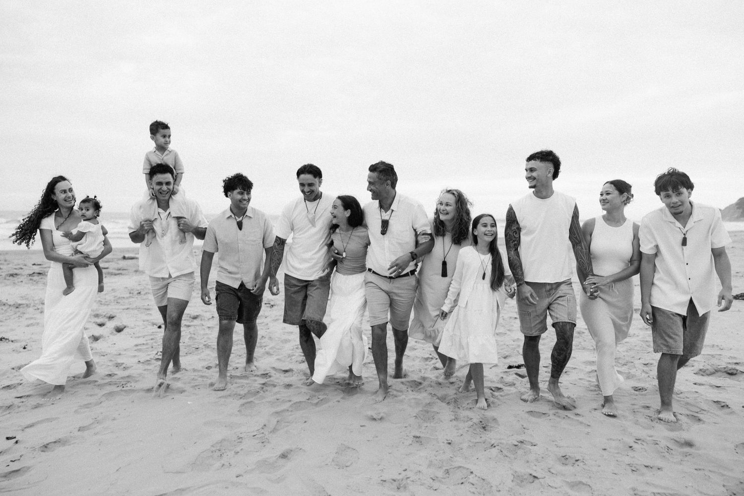 Family members walking together on a beach wearing coordinated white and neutral colored outfits.