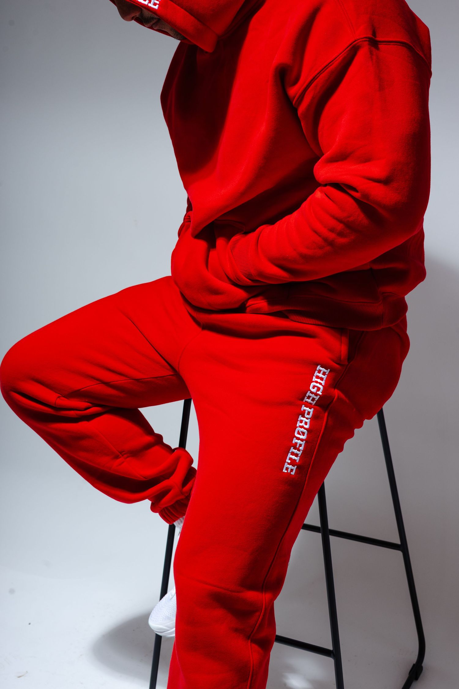 Person wearing bright red streetwear sweatsuit sitting on a stool against gray background.