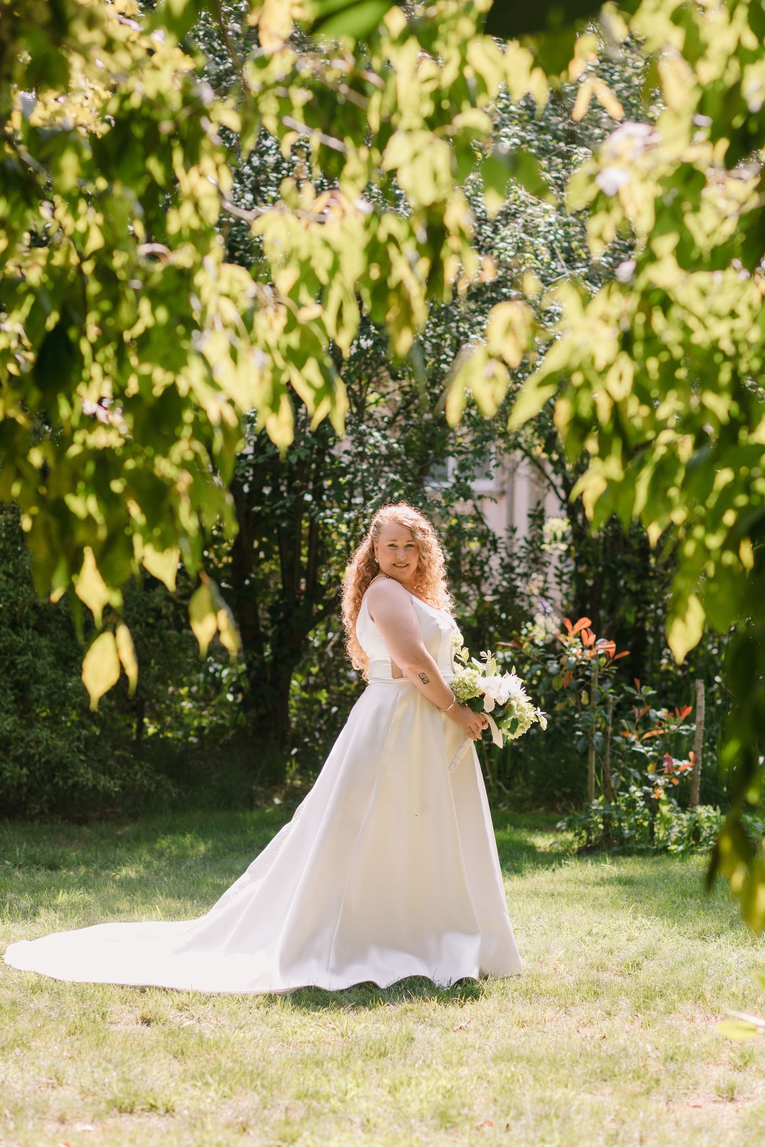 A bride in a flowing white wedding dress twirls in a sunlit garden setting with dreamy bokeh effects.