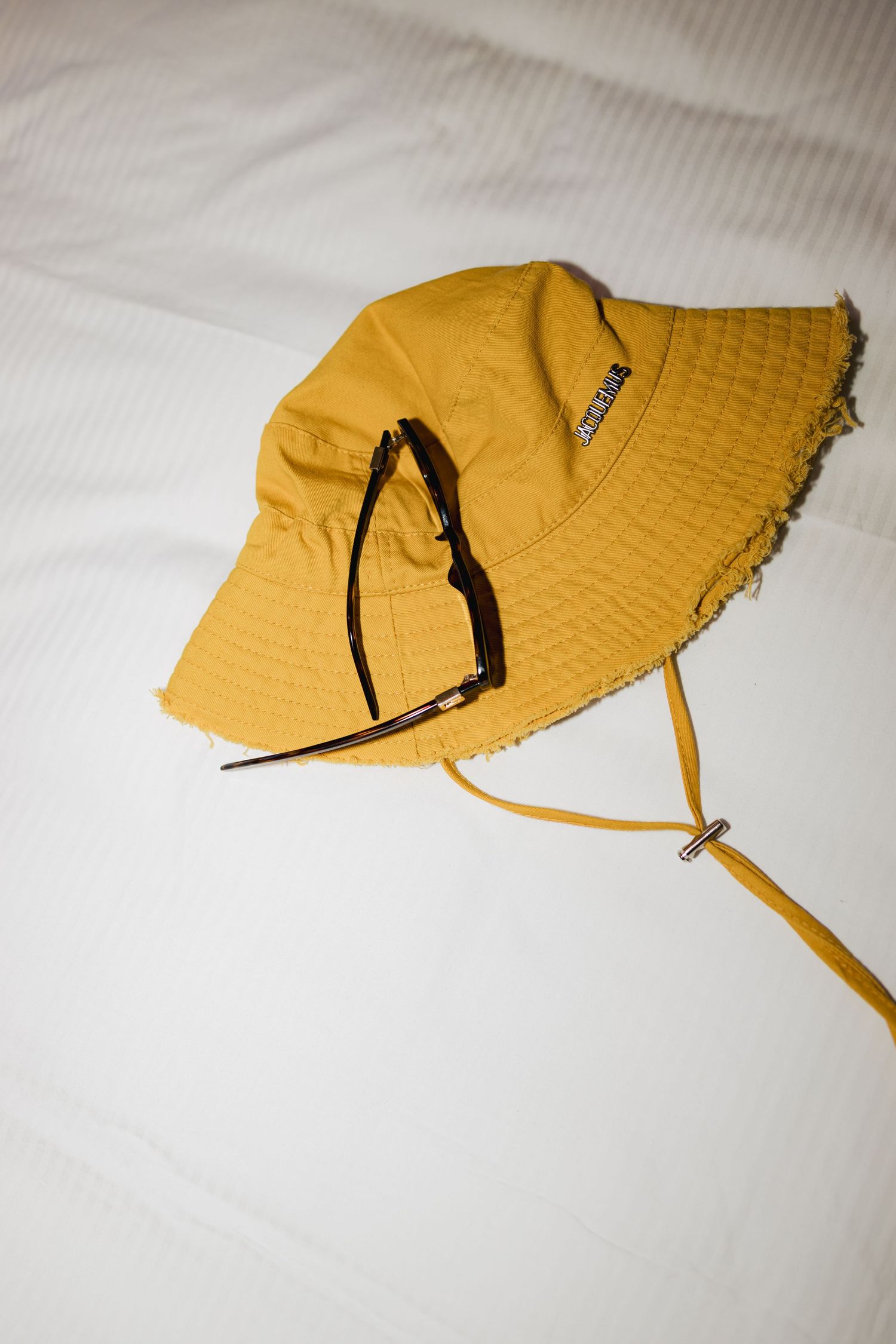 Yellow bucket hat with drawstring chin strap on white background.