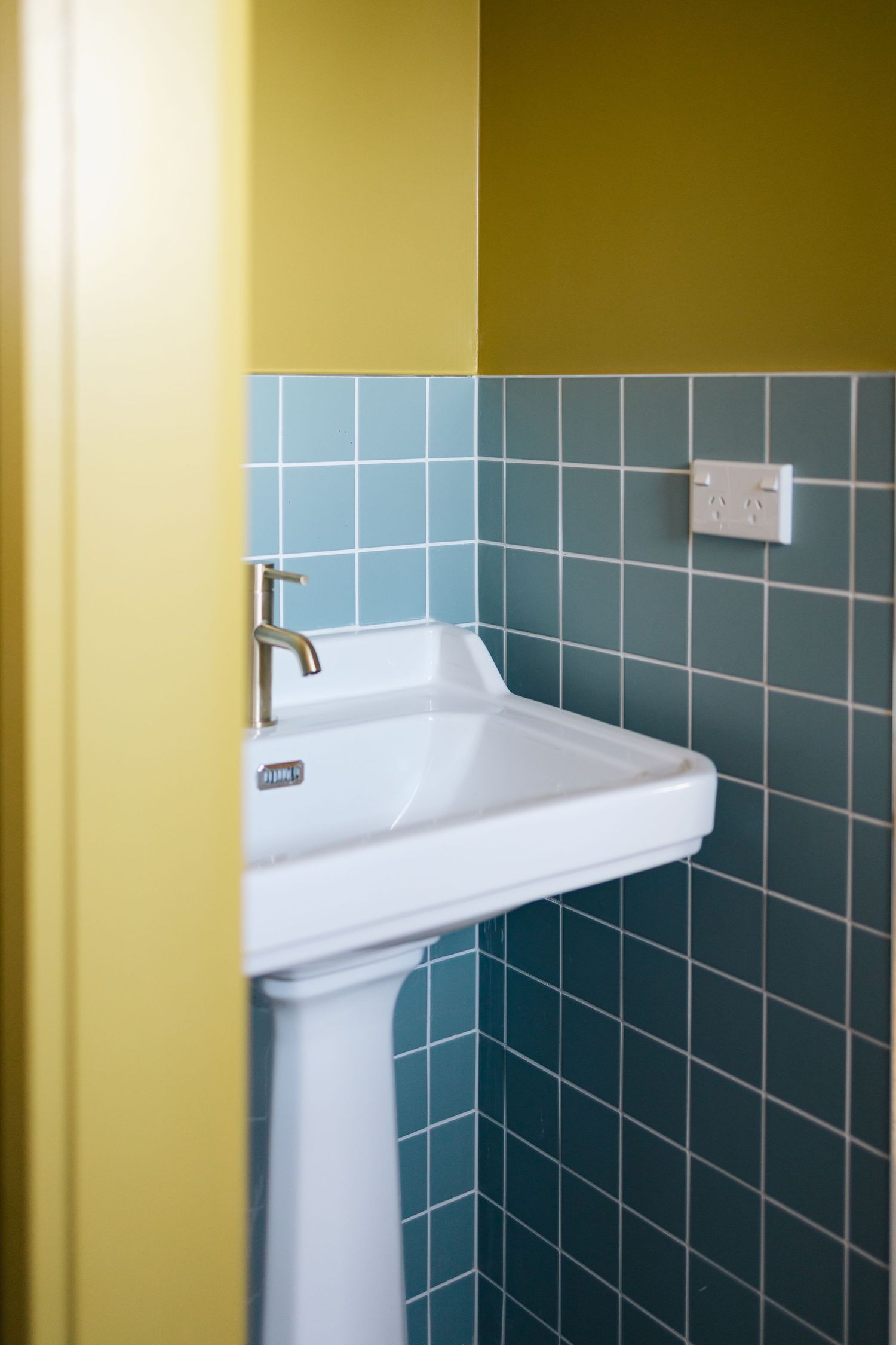 Modern bathroom interior with blue tile wall and white pedestal sink.