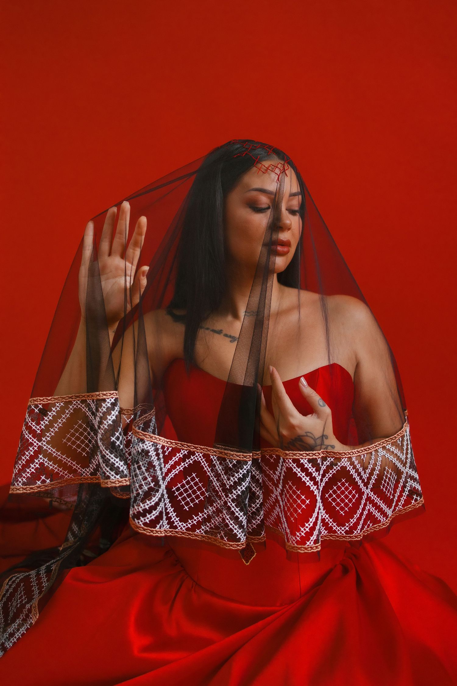 A model wearing a strapless red dress with lace trim poses dramatically against a red background.