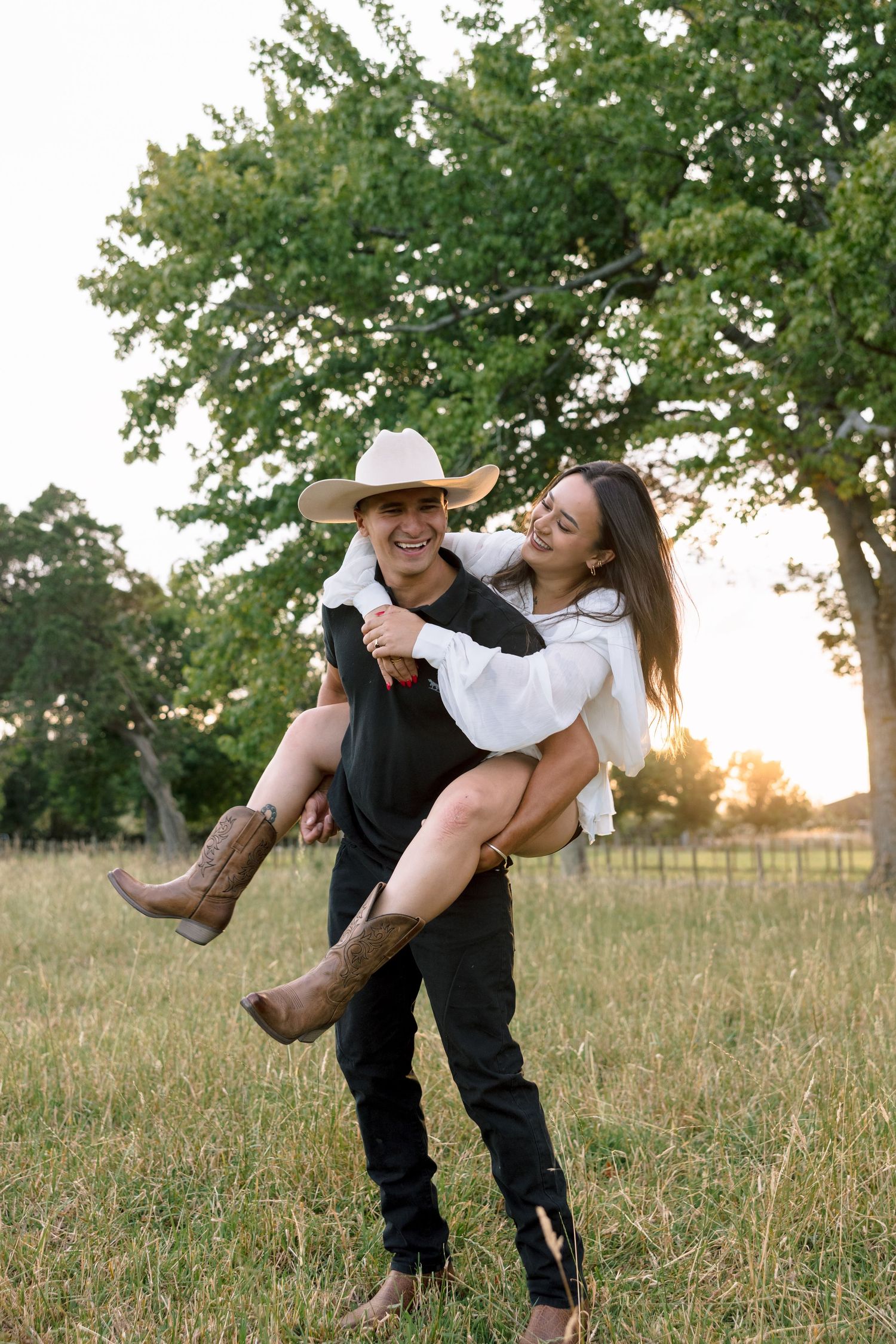 A couple playfully poses in a grassy field during golden hour with trees in the background.