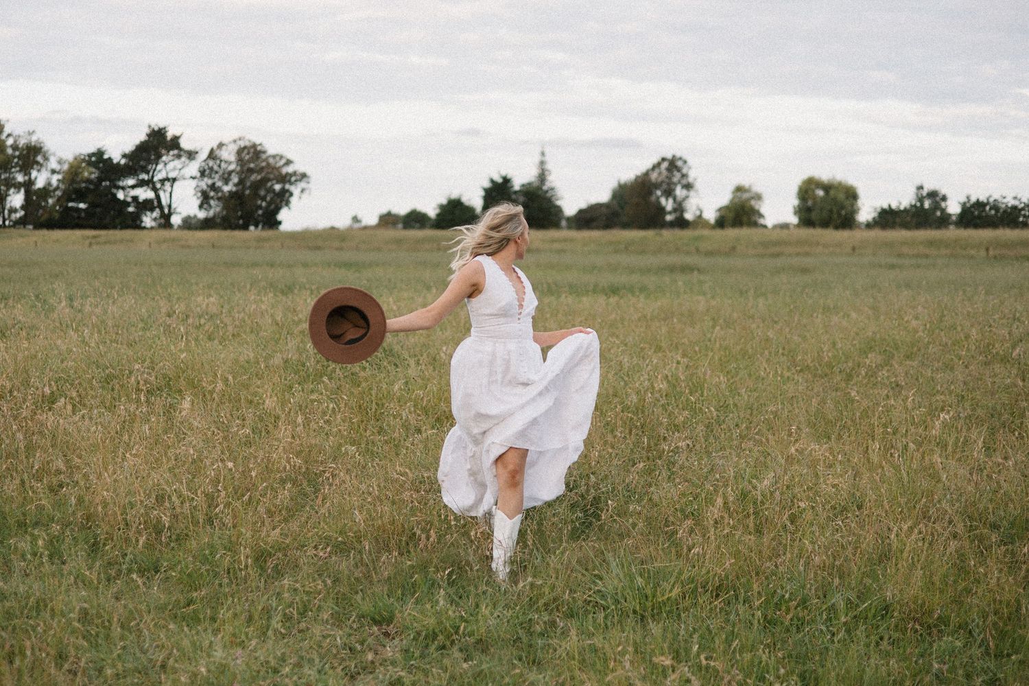 A person in a flowing white dress twirls gracefully in a green meadow field during a golden sunset.