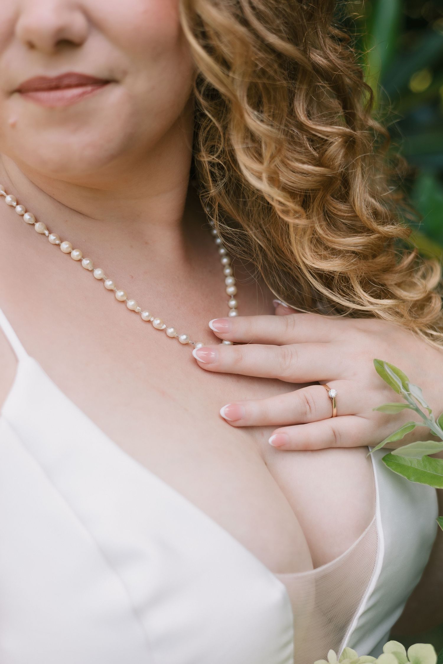 Detail shot of pearl necklace and ring with blonde curls and white dress.