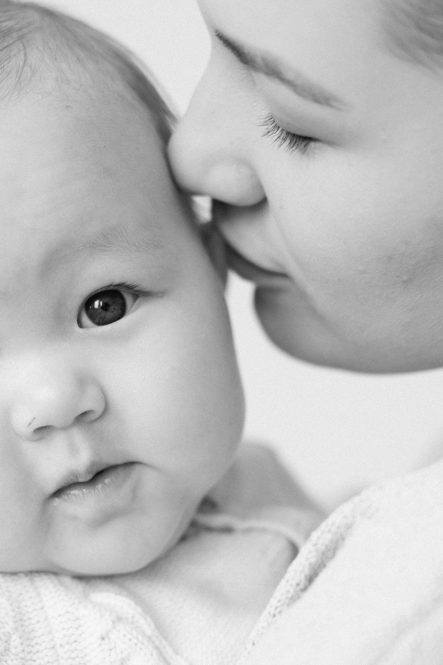 Black and white photo of a mother gently kissing her newborn baby on the head in a tender moment.