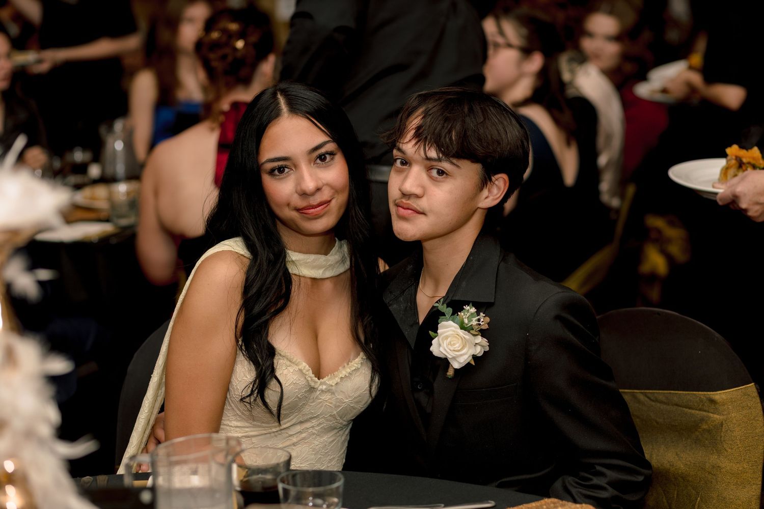 Young couple in formal attire posing together at prom, wearing corsage and white dress at banquet.