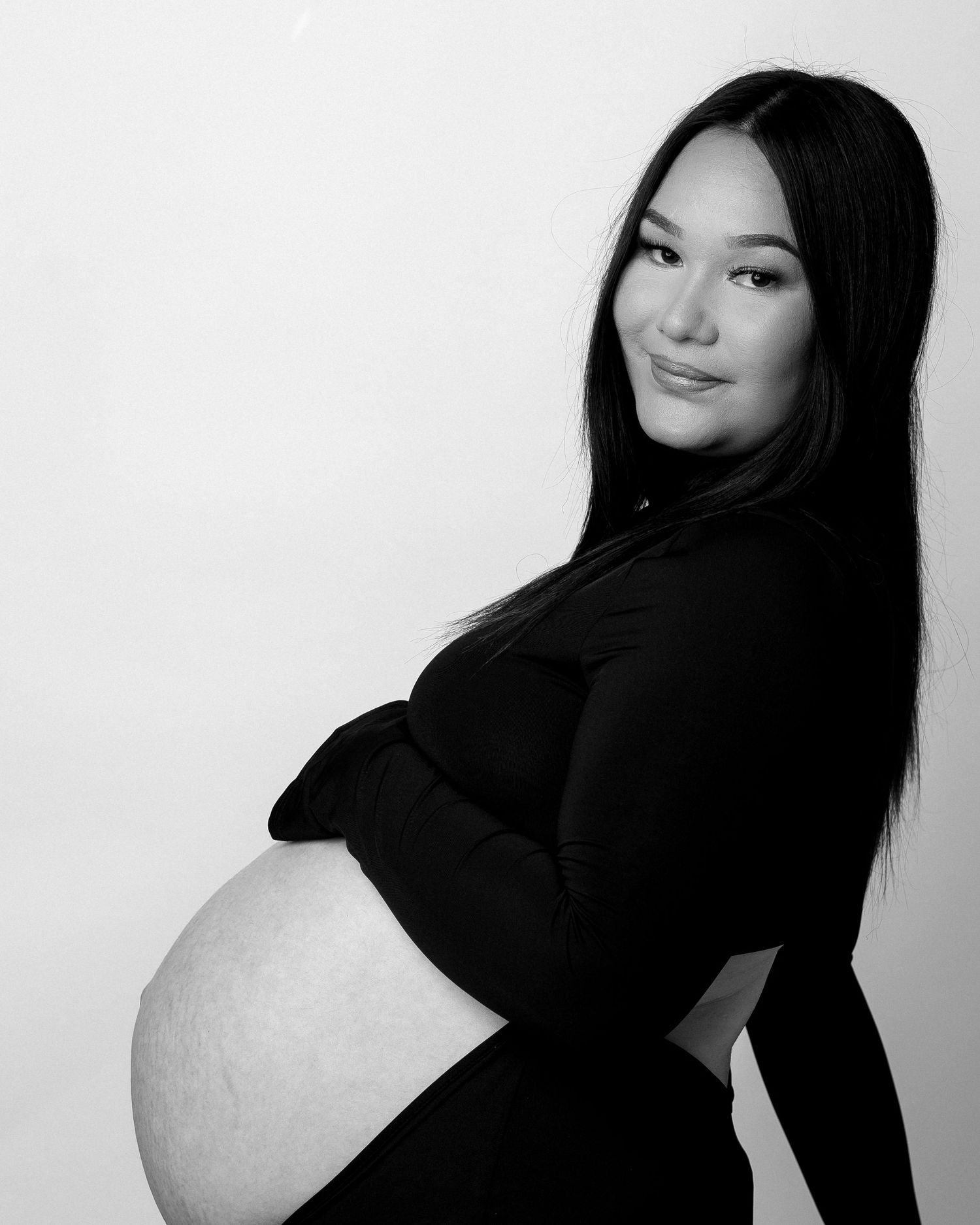 Black and white maternity portrait of a smiling pregnant woman in a black outfit, showcasing her baby bump.