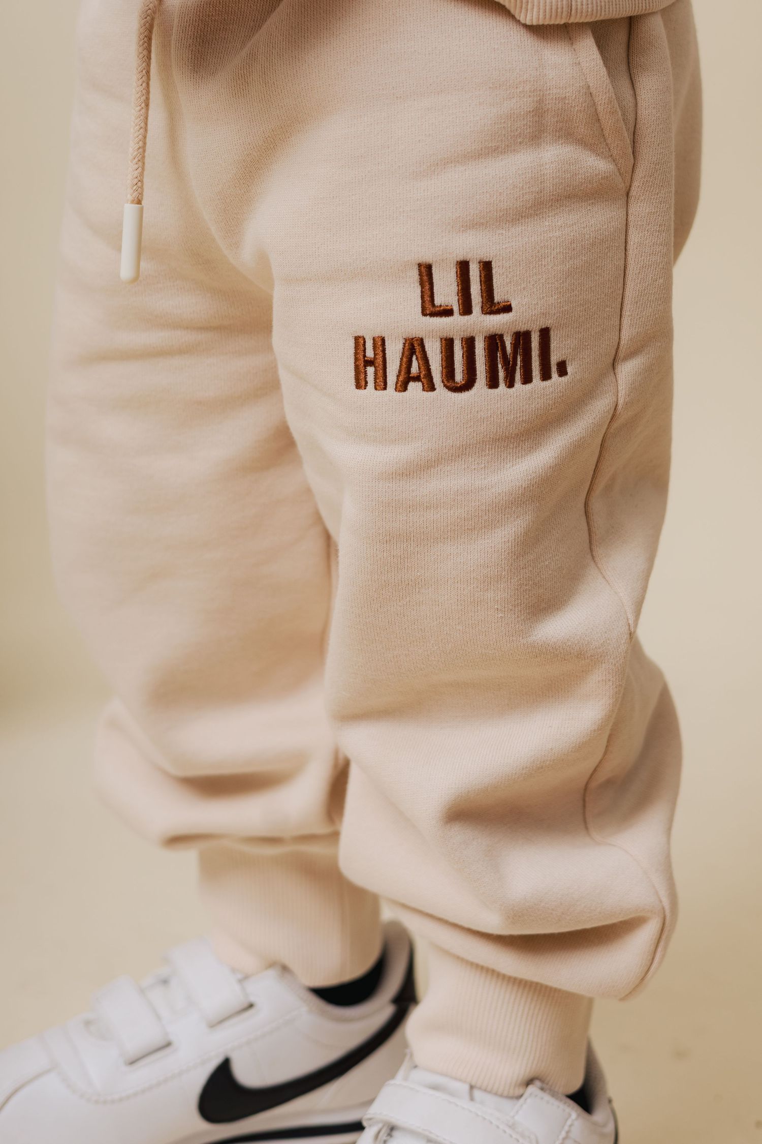 Close-up view of cream-colored sweatpants with Nike sneakers against a light beige background.