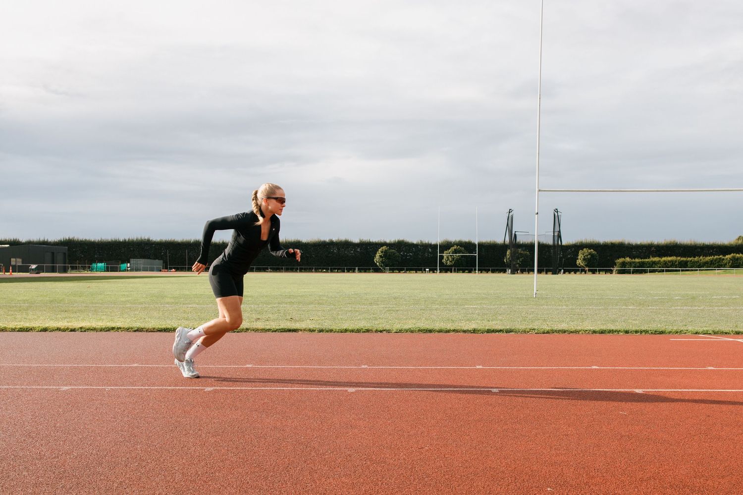 Athletic runner sprinting on a red running track during outdoor training session on cloudy day.