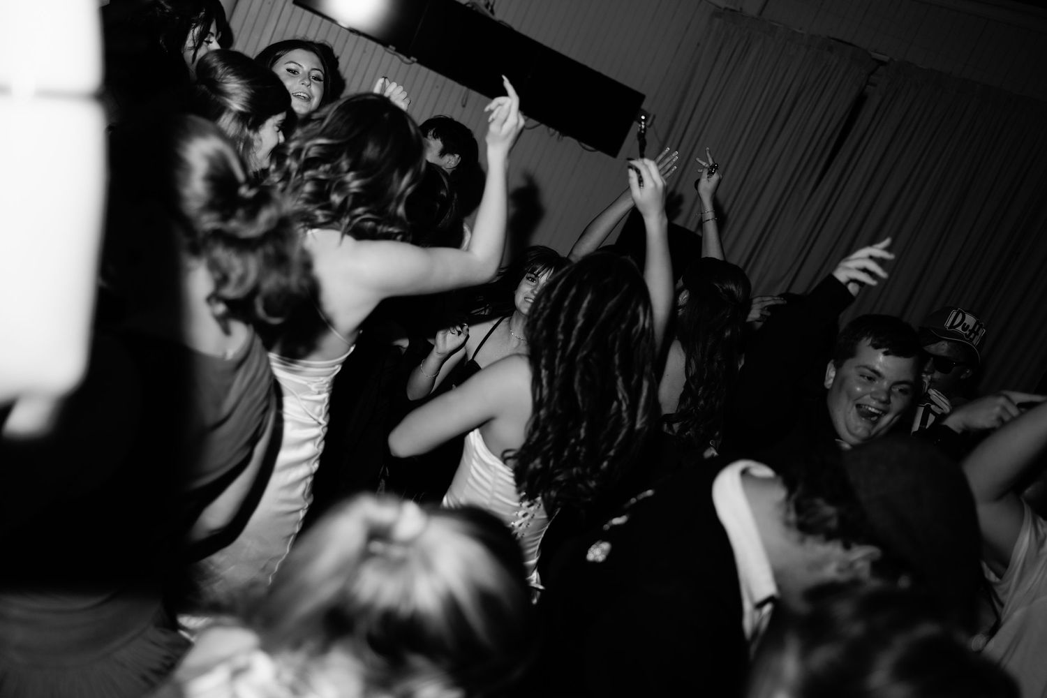 Black and white photo of guests dancing energetically at a lively wedding reception party.
