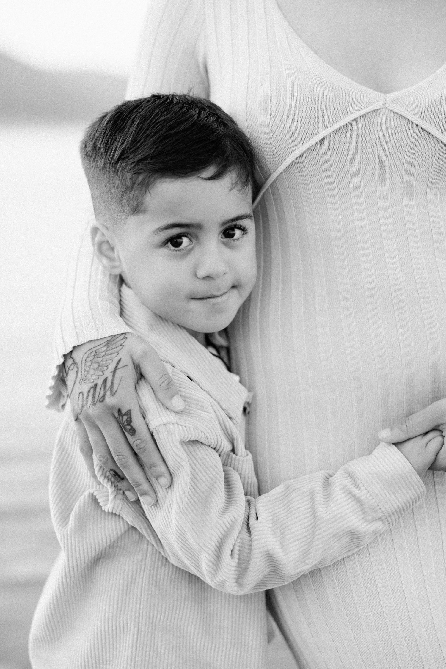 Black and white photo of a young boy hugging his mother tightly, looking at the camera with a sweet smile.