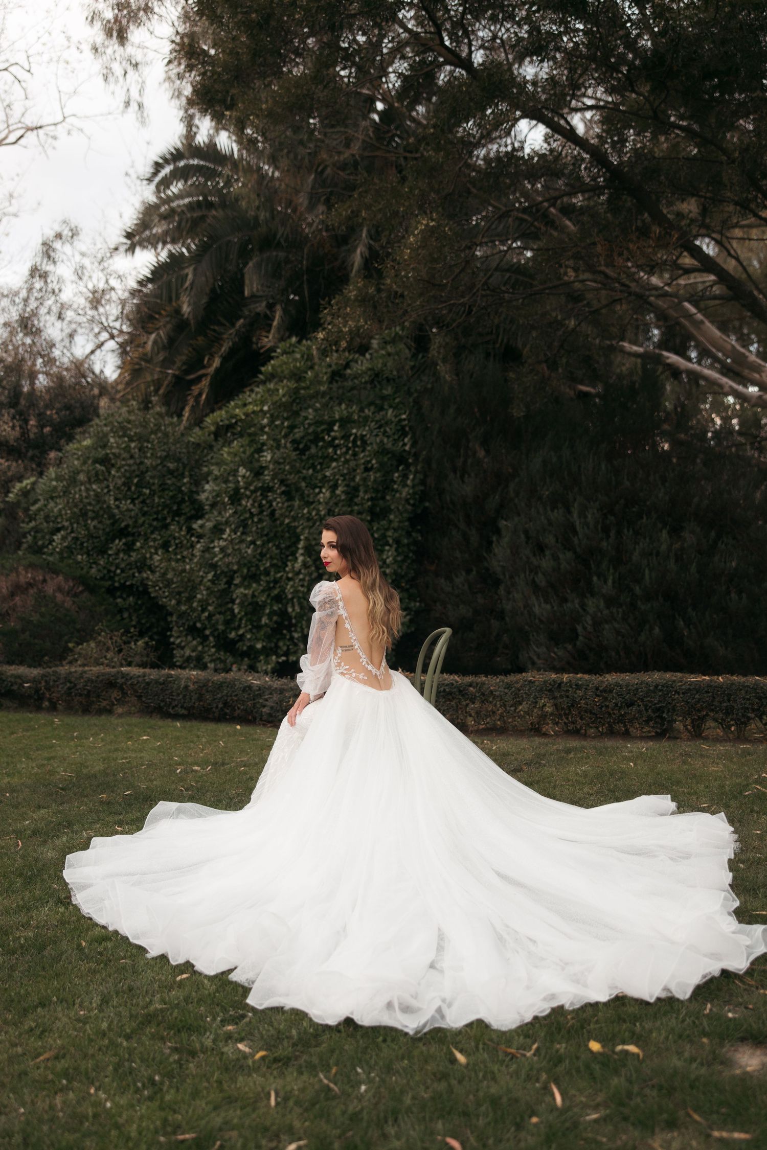 Dreamy bridal portrait of a flowing white wedding dress with long train against a dark garden backdrop.