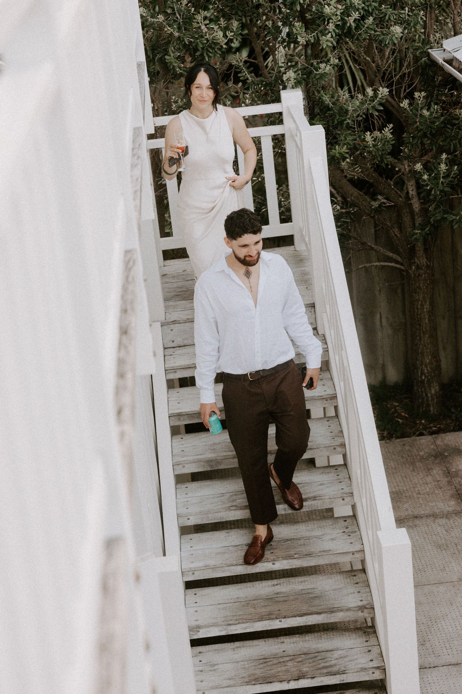 Person in white shirt and brown pants walking down white wooden stairs outdoors.