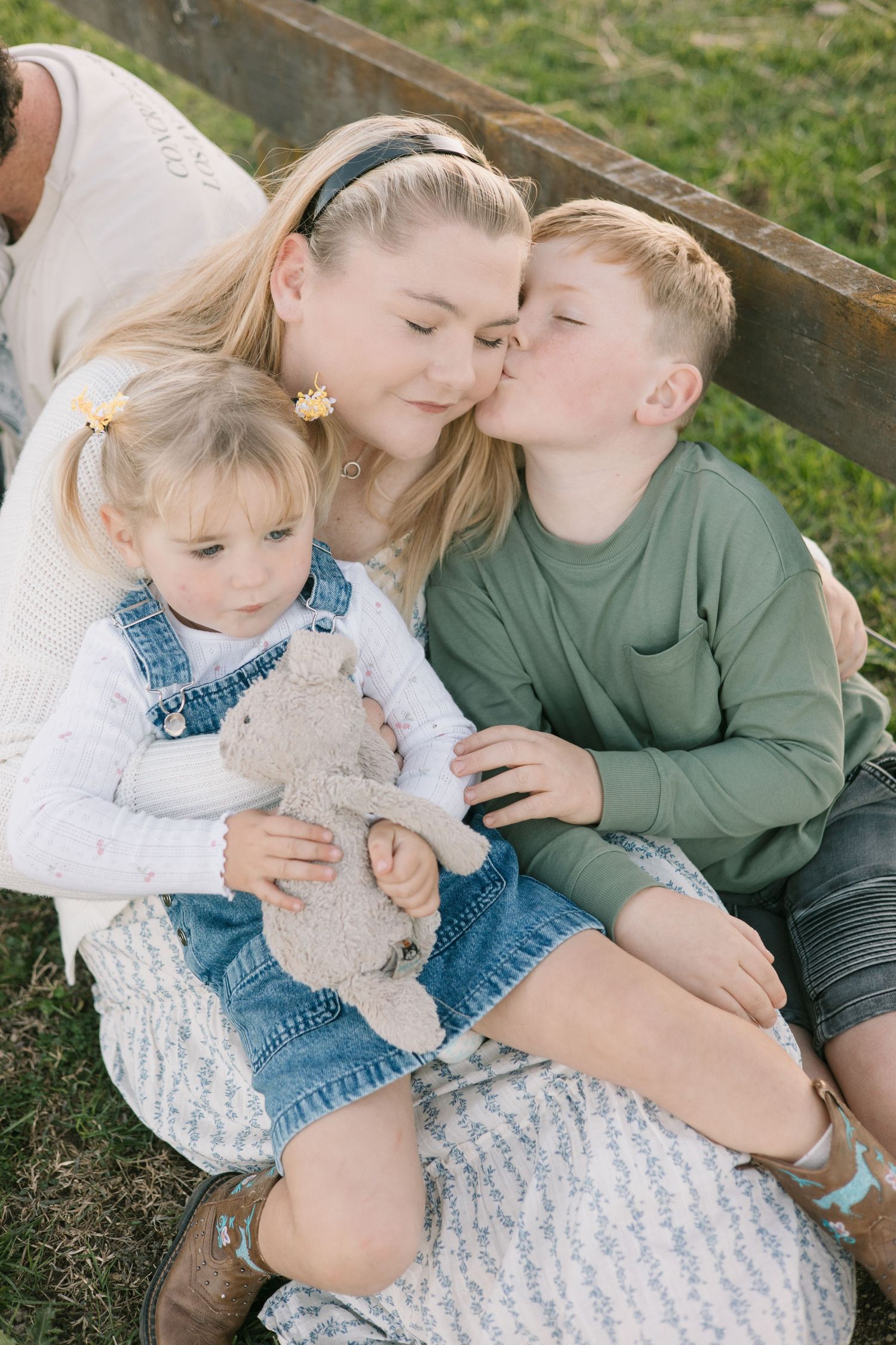 Family sitting together outdoors on grass sharing tender moments with a plush teddy bear.