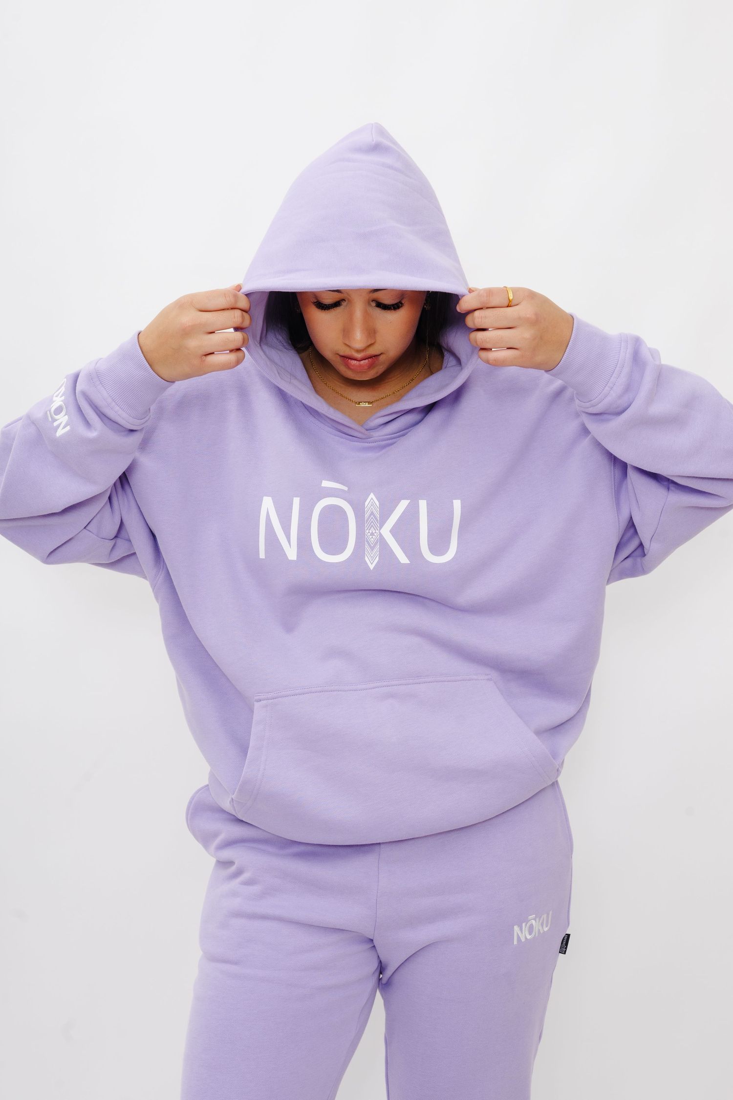 Person wearing a lavender colored NOKU branded sweatsuit lounging in various poses against white background.