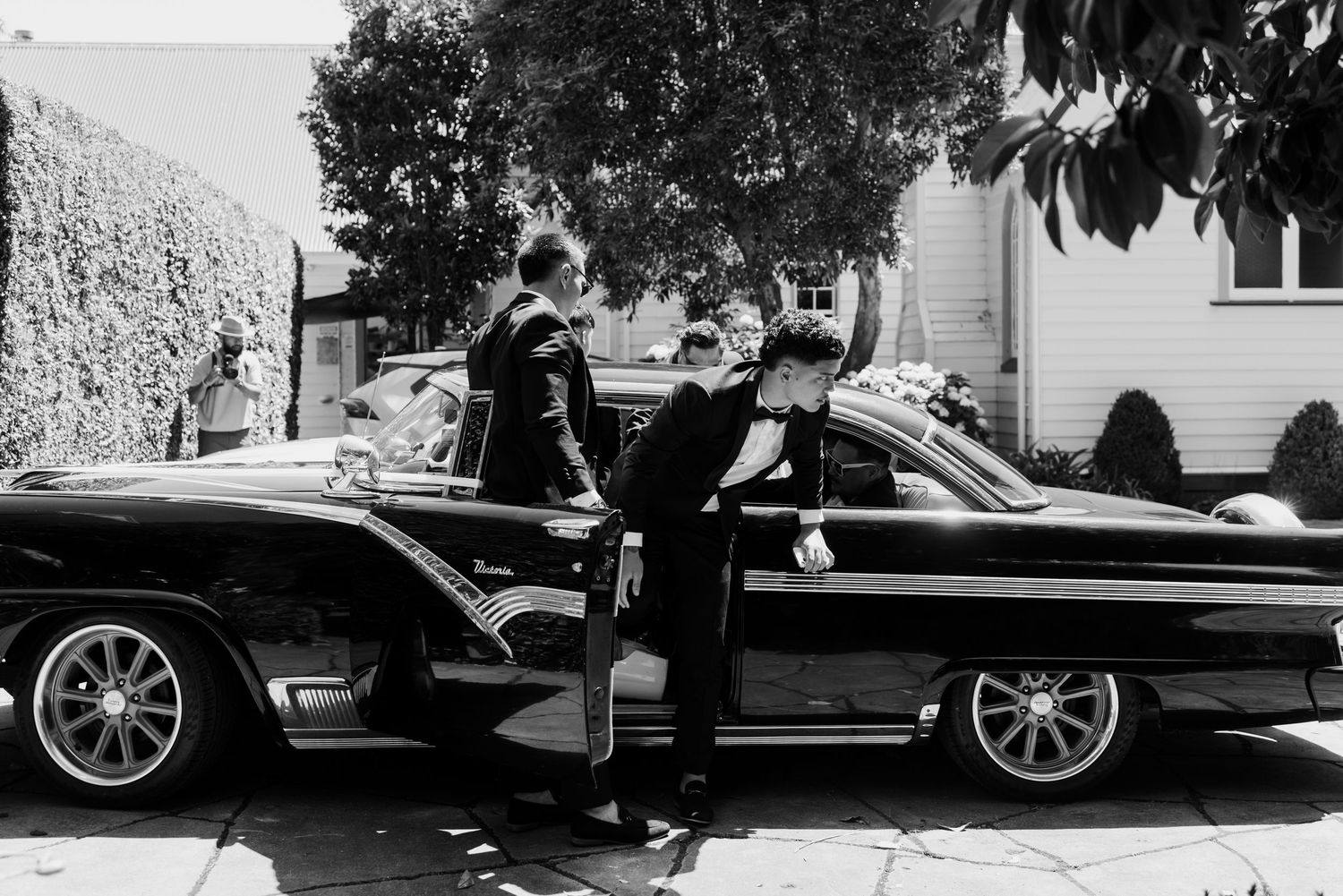 A black vintage car parked under trees on a residential street.