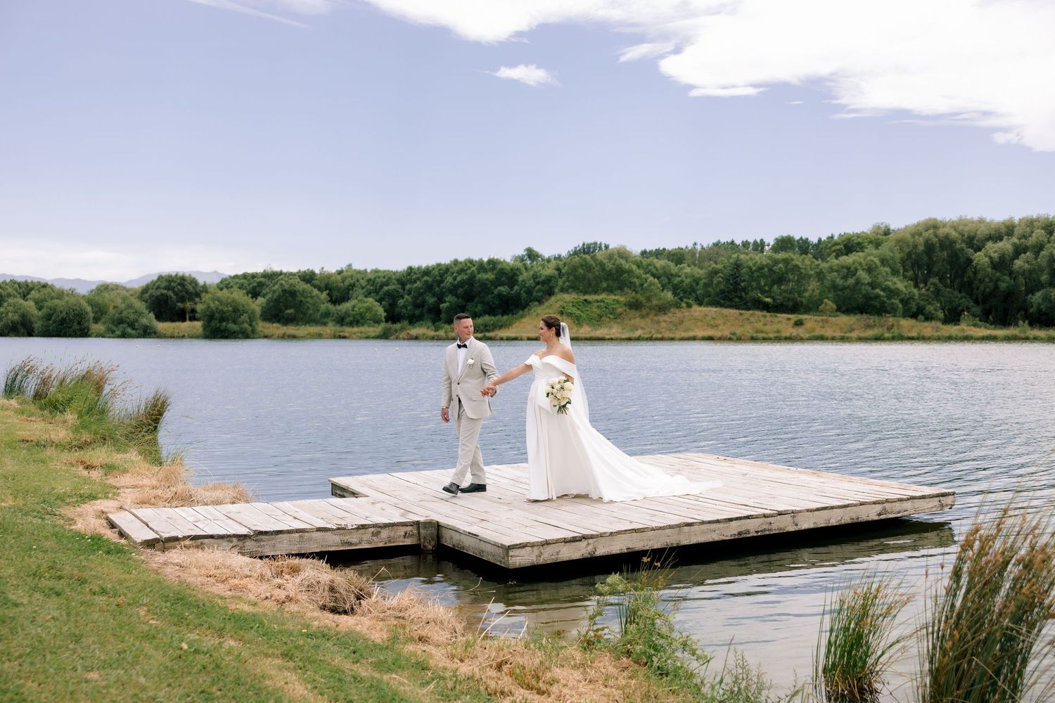 A serene lakeside dock stretches into calm waters surrounded by green shoreline on a sunny summer day.