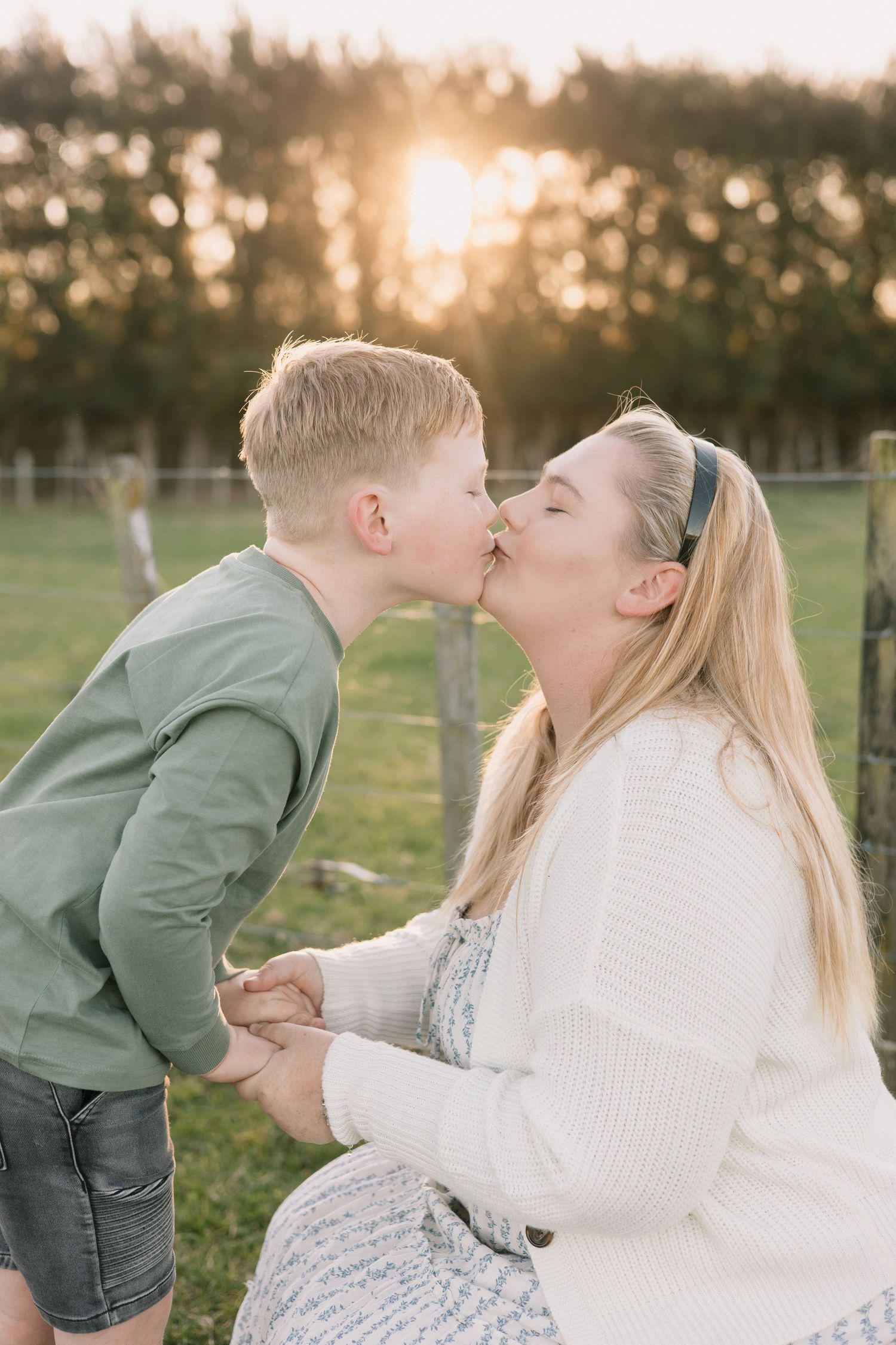 A sweet family moment captured at sunset in a grassy field with warm golden lighting.