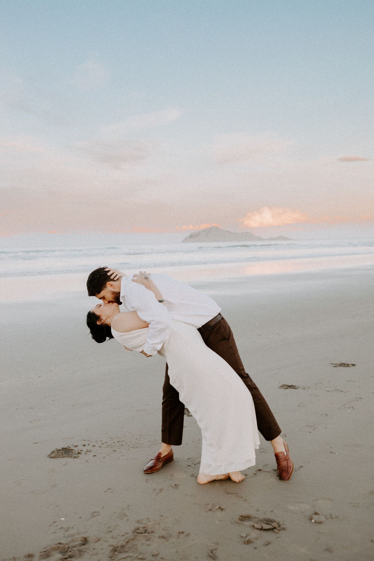 A couple embraces in a romantic dance pose on a misty beach at sunset.