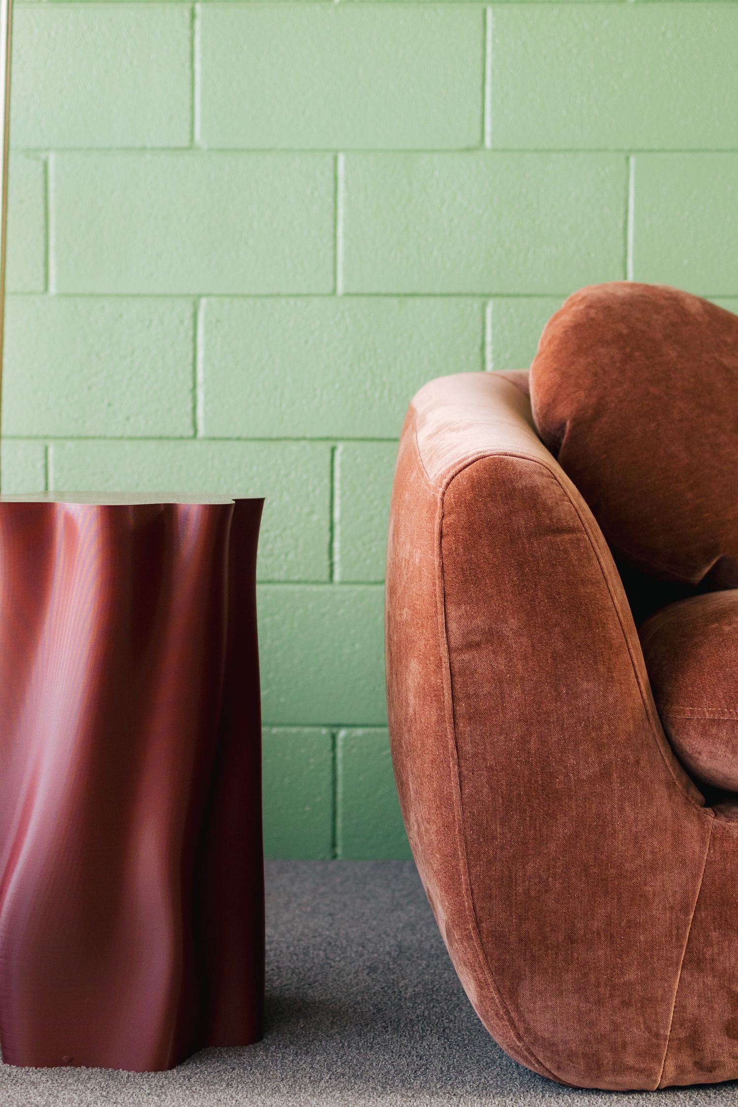 Brown velvet armchair against mint green brick wall with red modern side table.