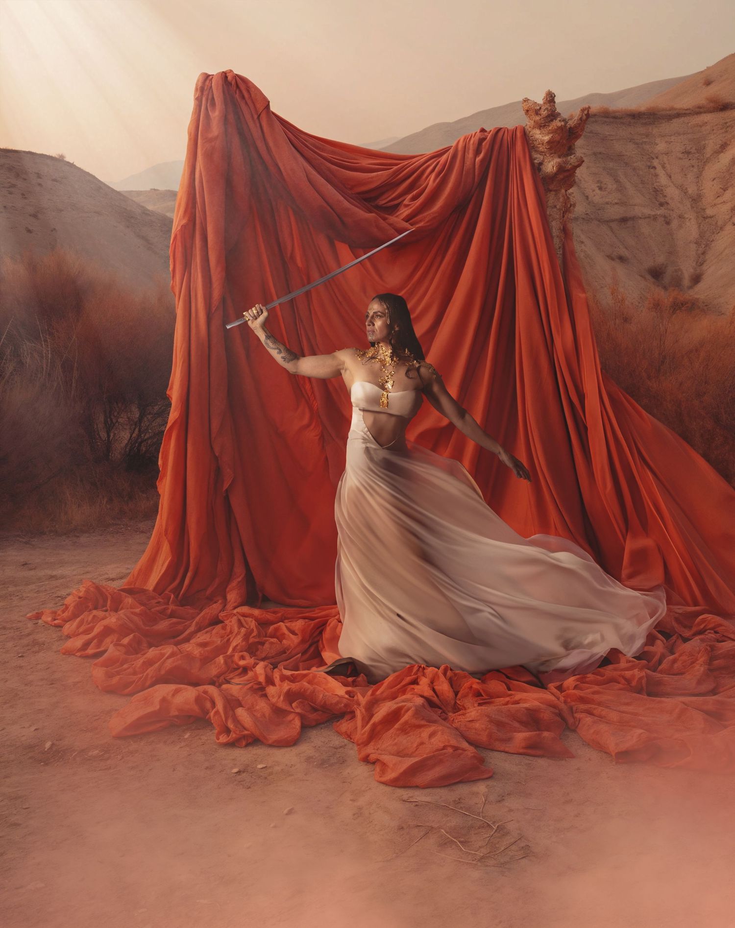 Artistic portrait in desert landscape with flowing red fabric backdrop and ethereal white dress creating dramatic atmosphere.