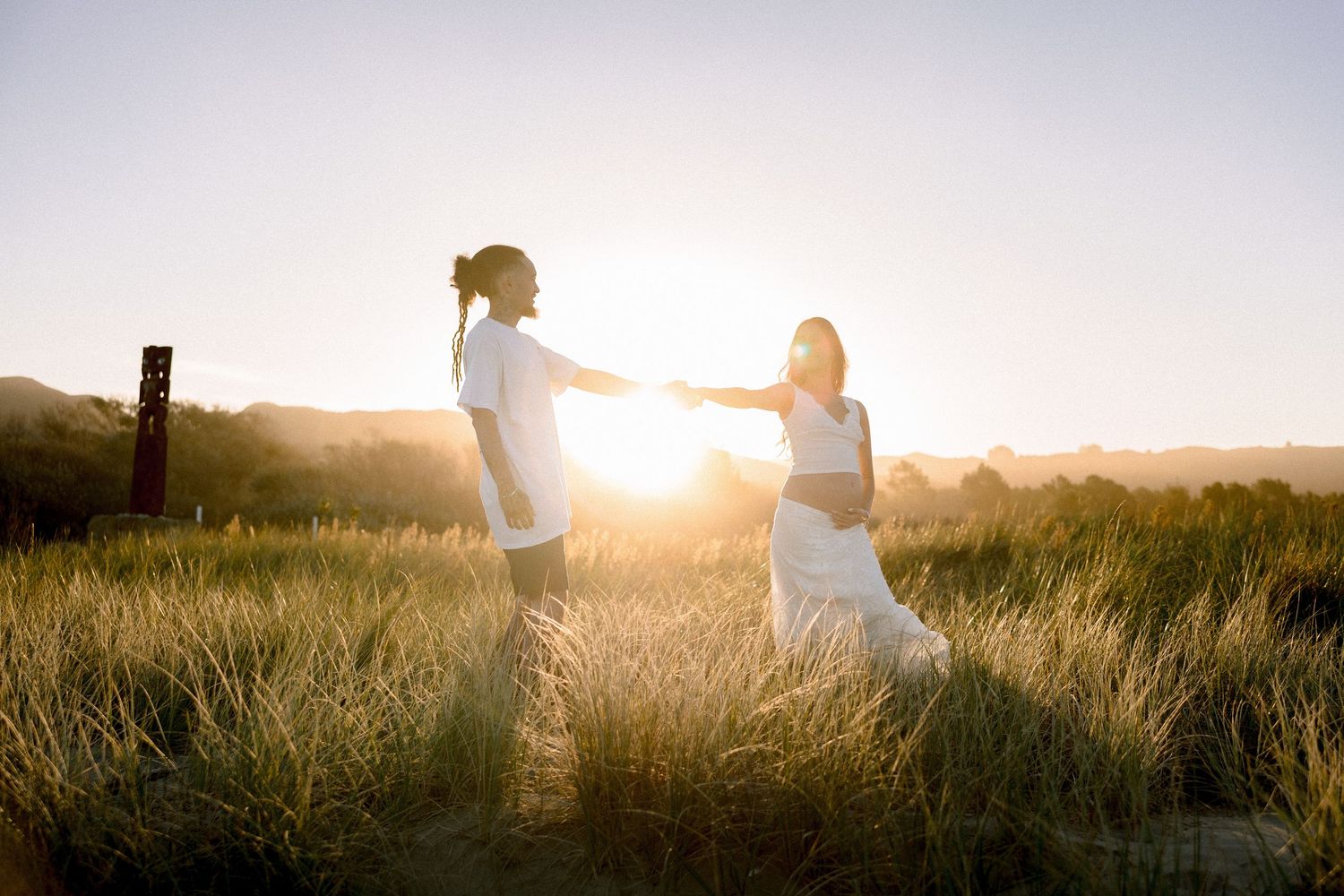 Couple holding hands in golden sunset light in a grassy field, romantic outdoor photography.
