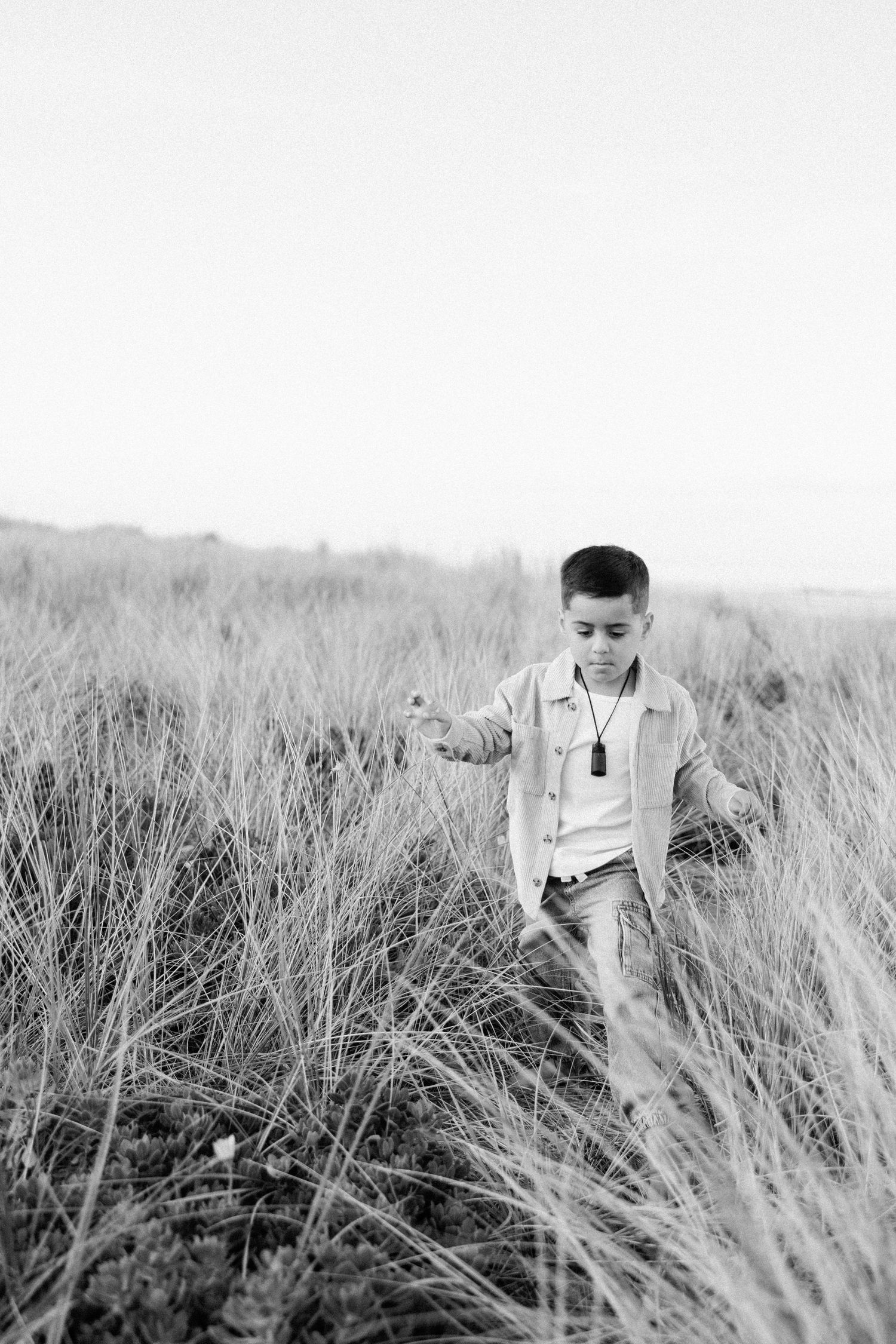 A young boy walks through tall grass in a black and white outdoor photo.