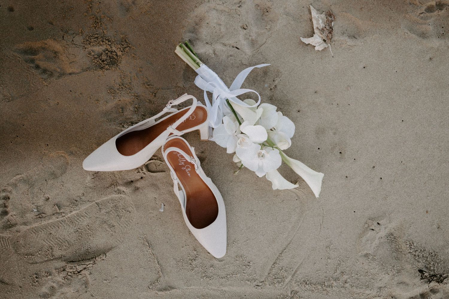 White bridal flats with laces displayed with delicate white orchids on concrete surface.