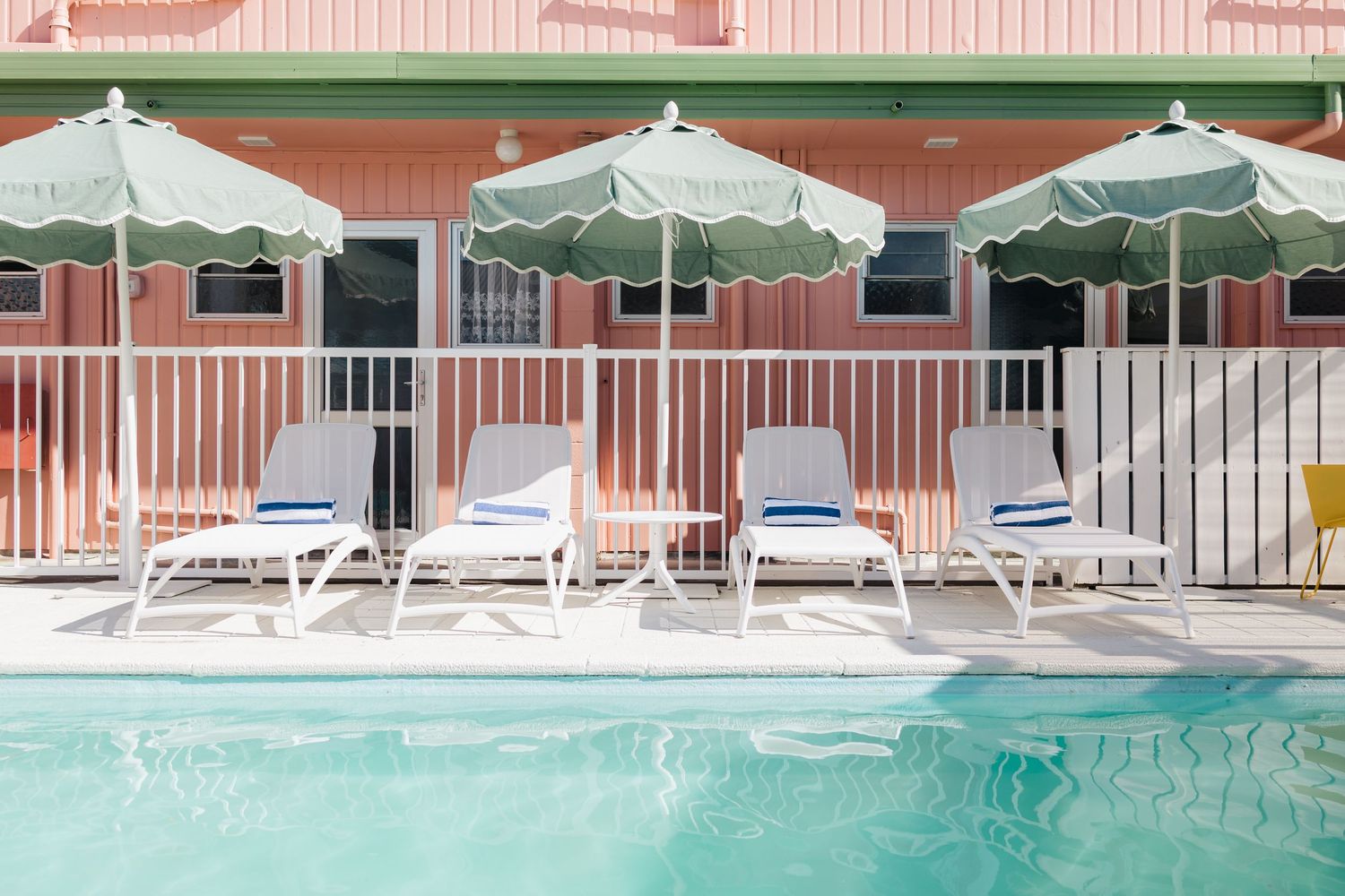 Retro motel poolside with white lounge chairs and mint green umbrellas.