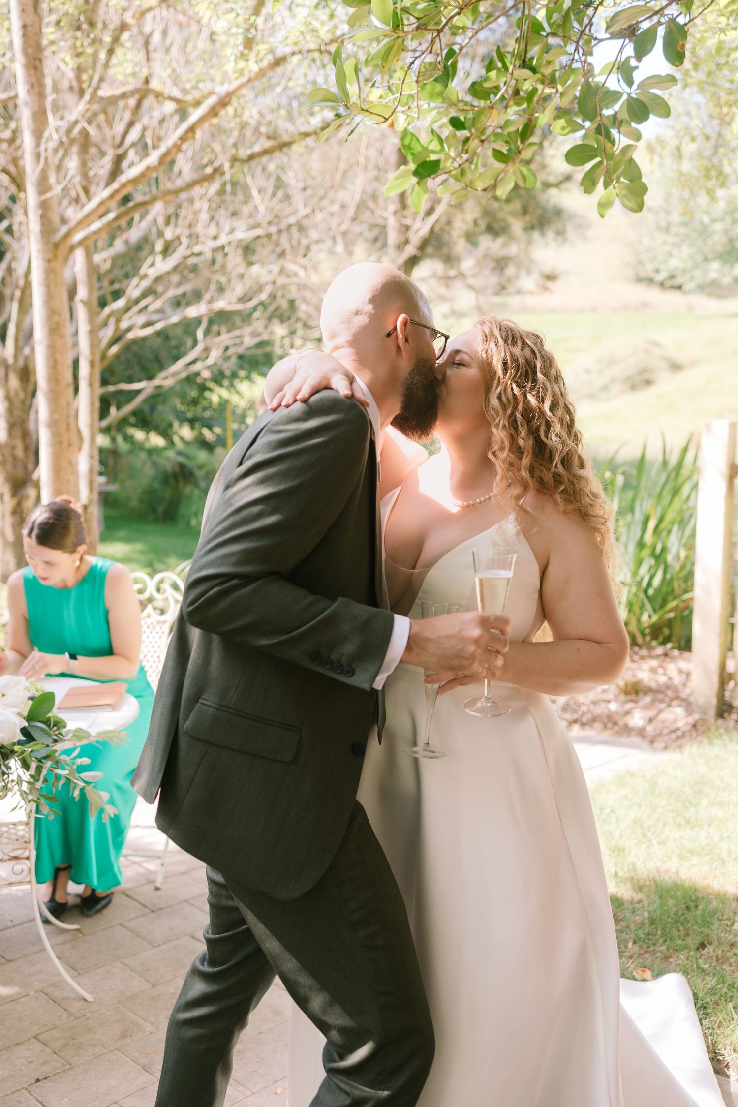Newlyweds share their first dance while holding champagne glasses in a garden setting.