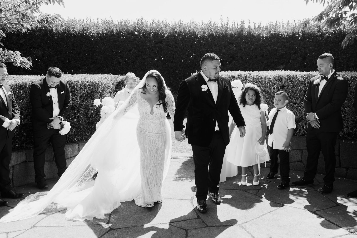 A black and white wedding photo sequence showing the bride and groom walking with their wedding party outdoors.