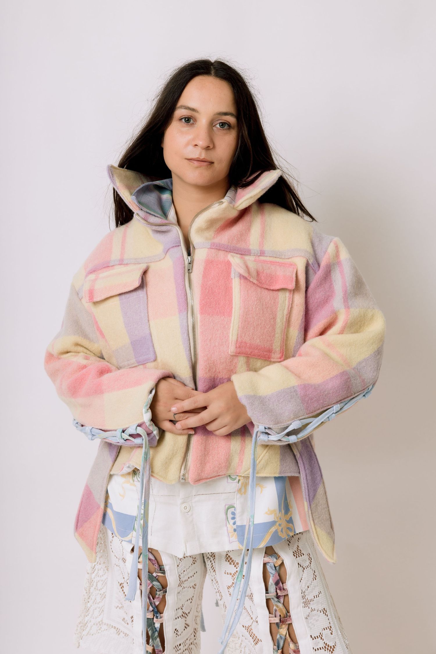 Person wearing a pastel patchwork fleece jacket with front pockets and zip closure poses against white background.