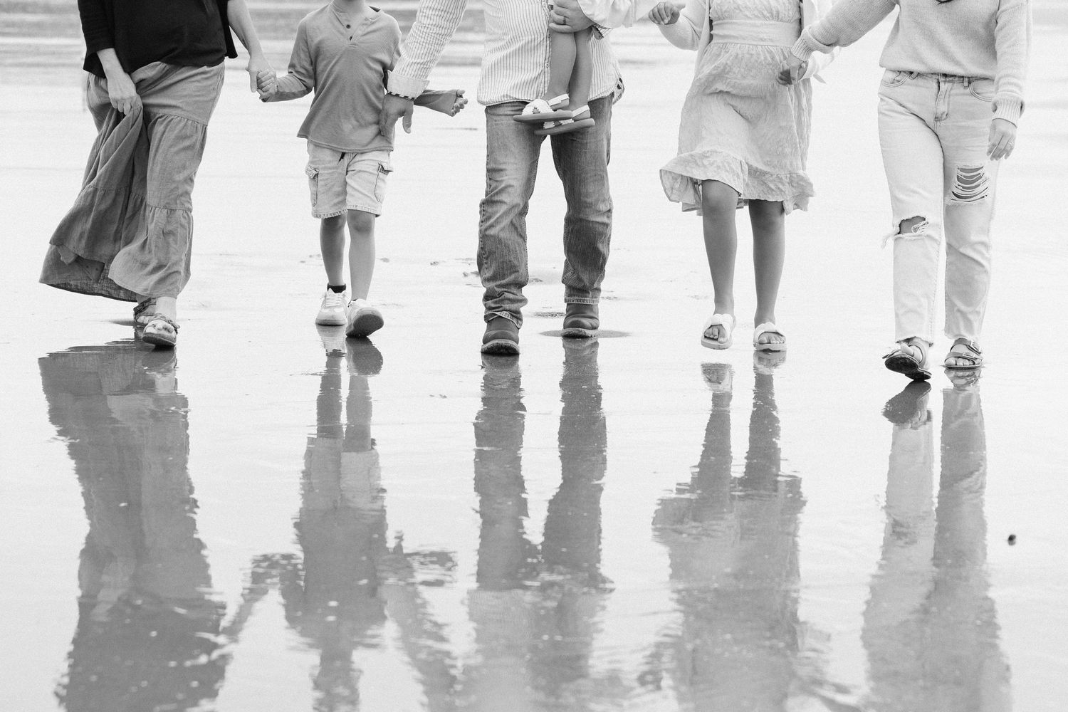 Black and white image of legs and feet walking on wet reflective surface creating mirror-like reflections below.