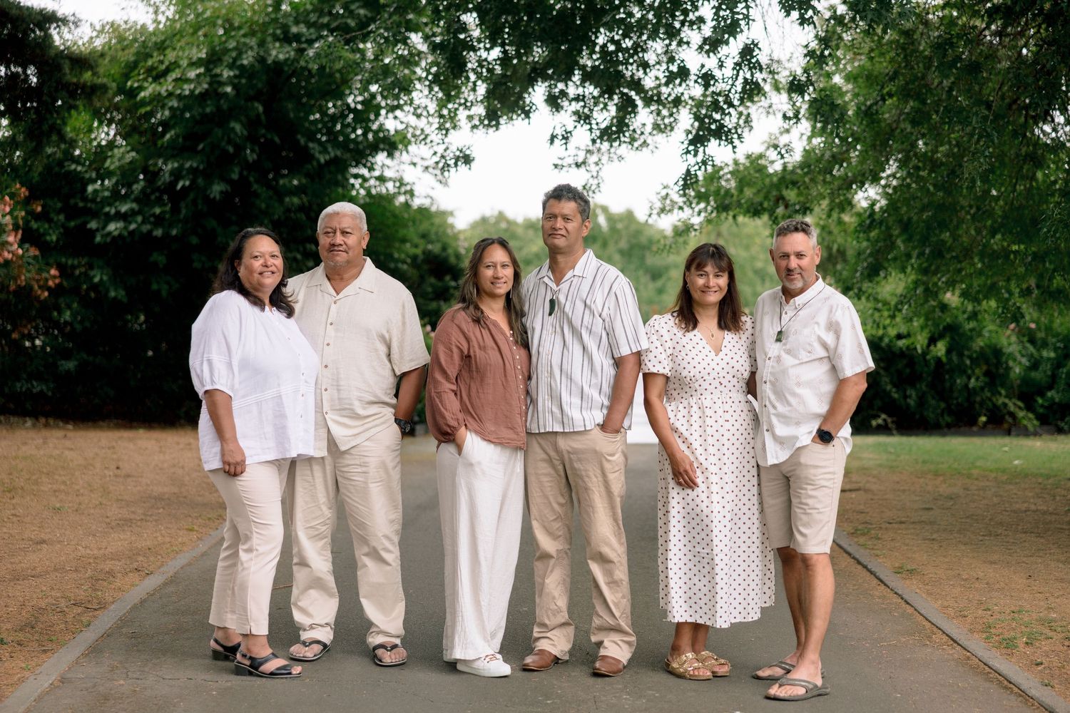 A group of people wearing white outfits pose together outdoors in a garden setting.