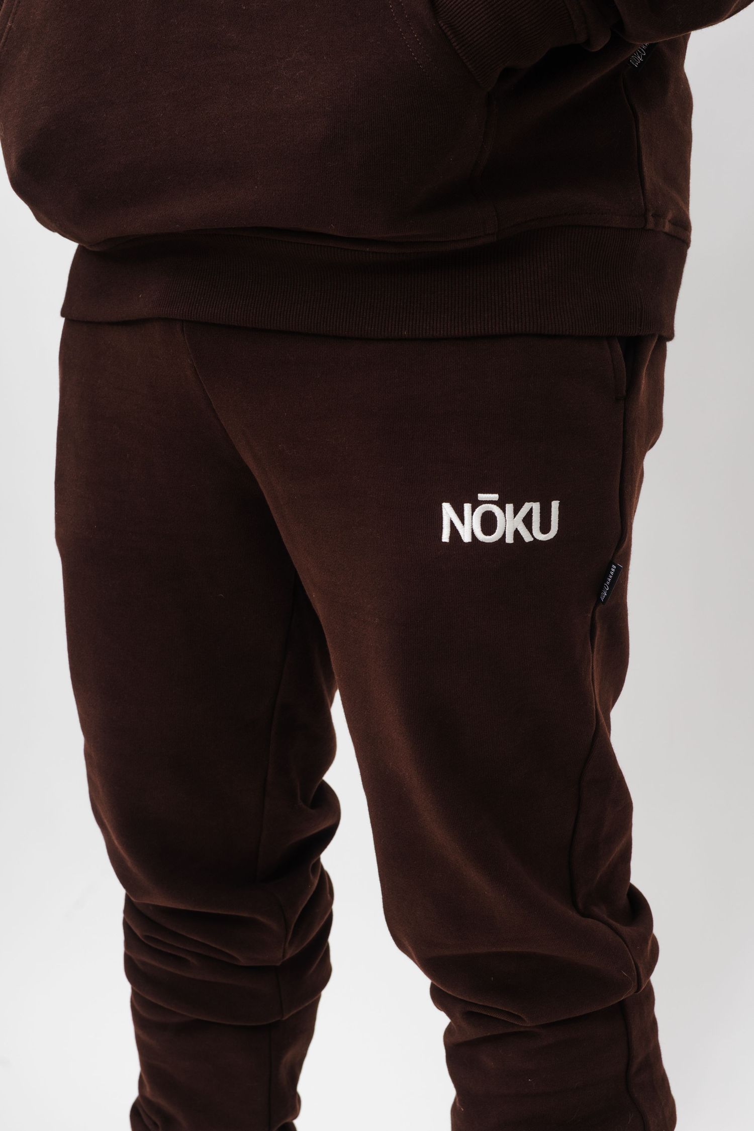 Close-up of brown athletic sweatpants with NOKU logo branding on the thigh.