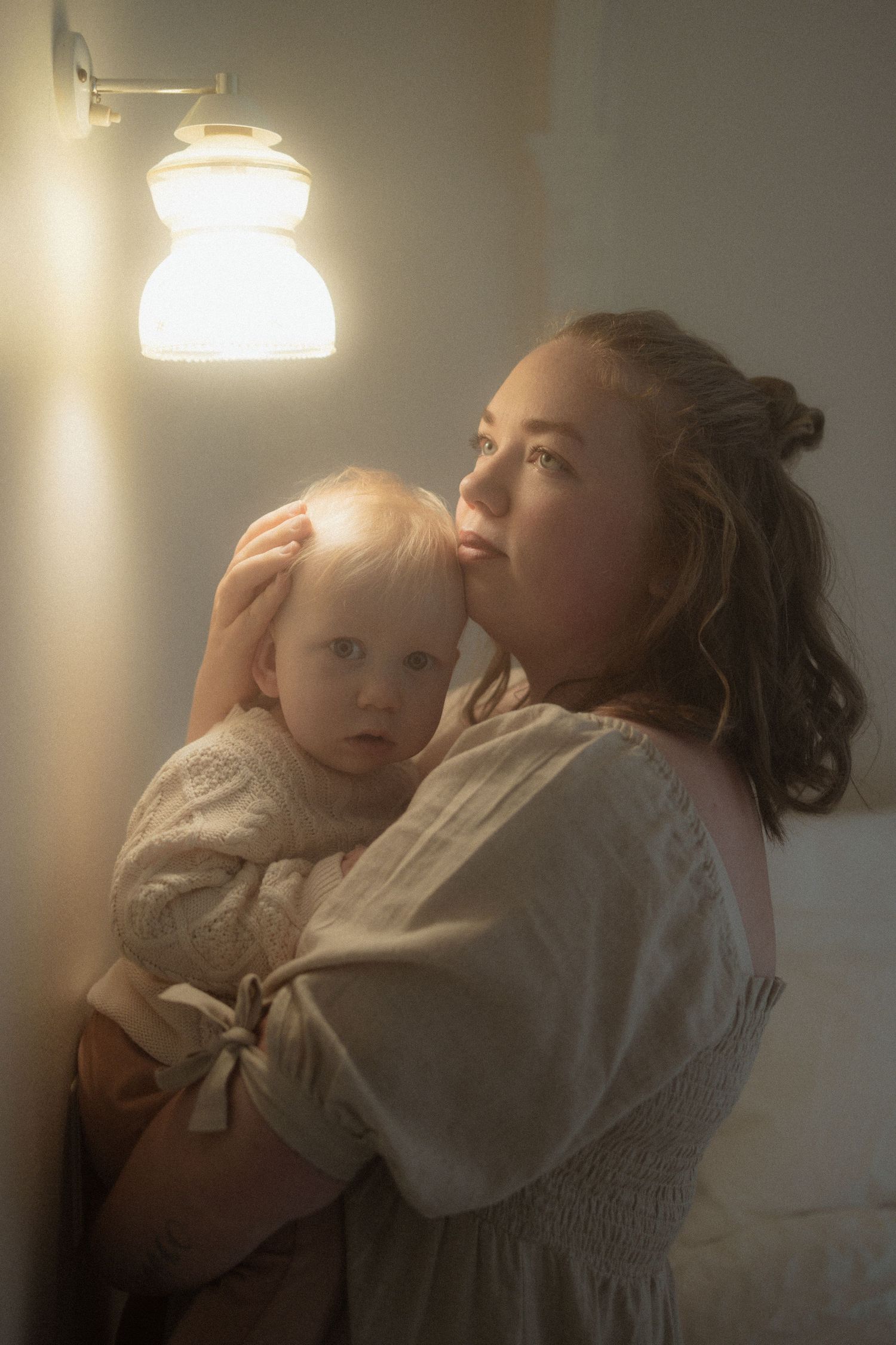 A tender moment captured in warm lighting as parent and child share a quiet embrace near a wall-mounted lamp.