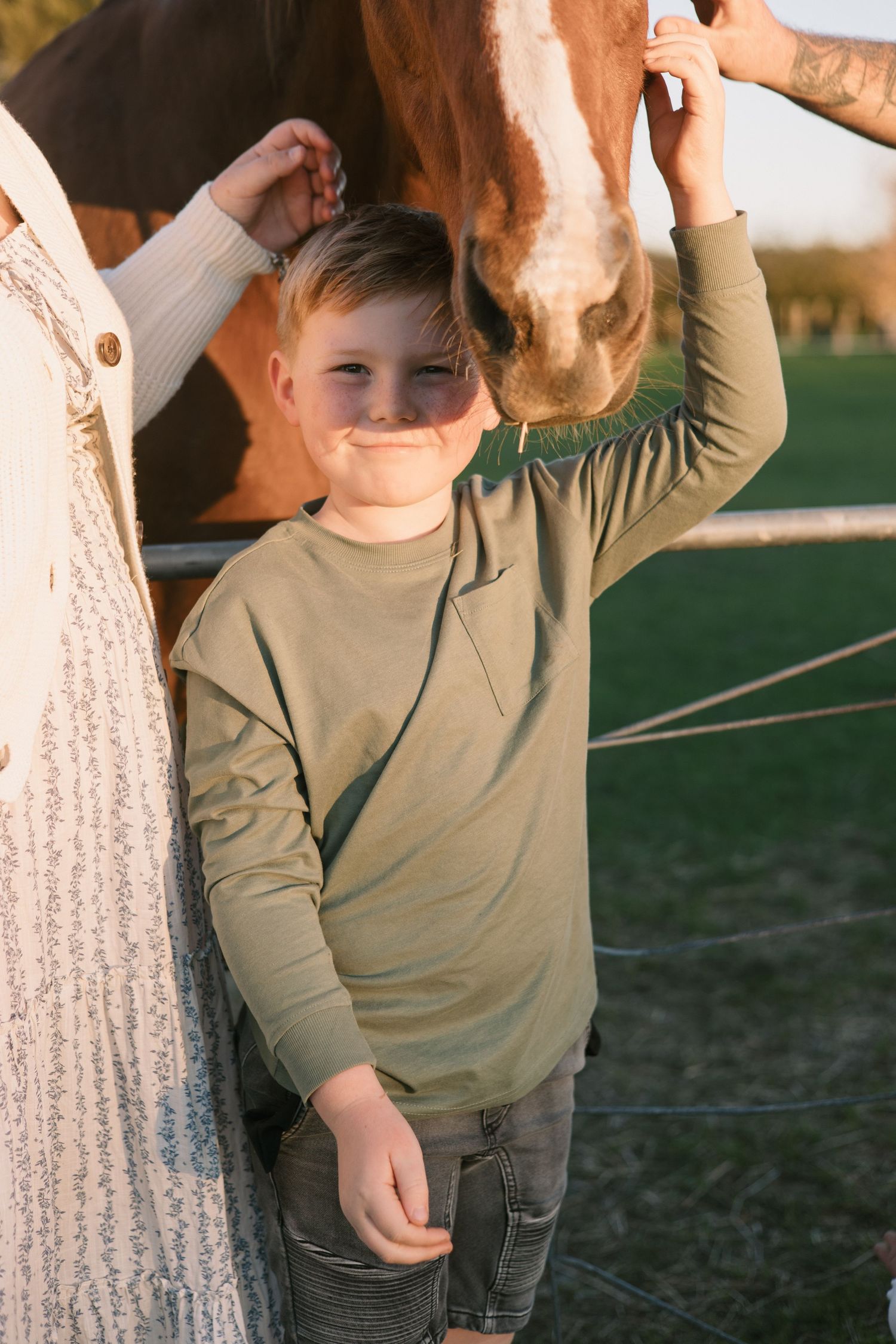A child wearing a tan long-sleeve shirt plays outdoors in warm sunlight.