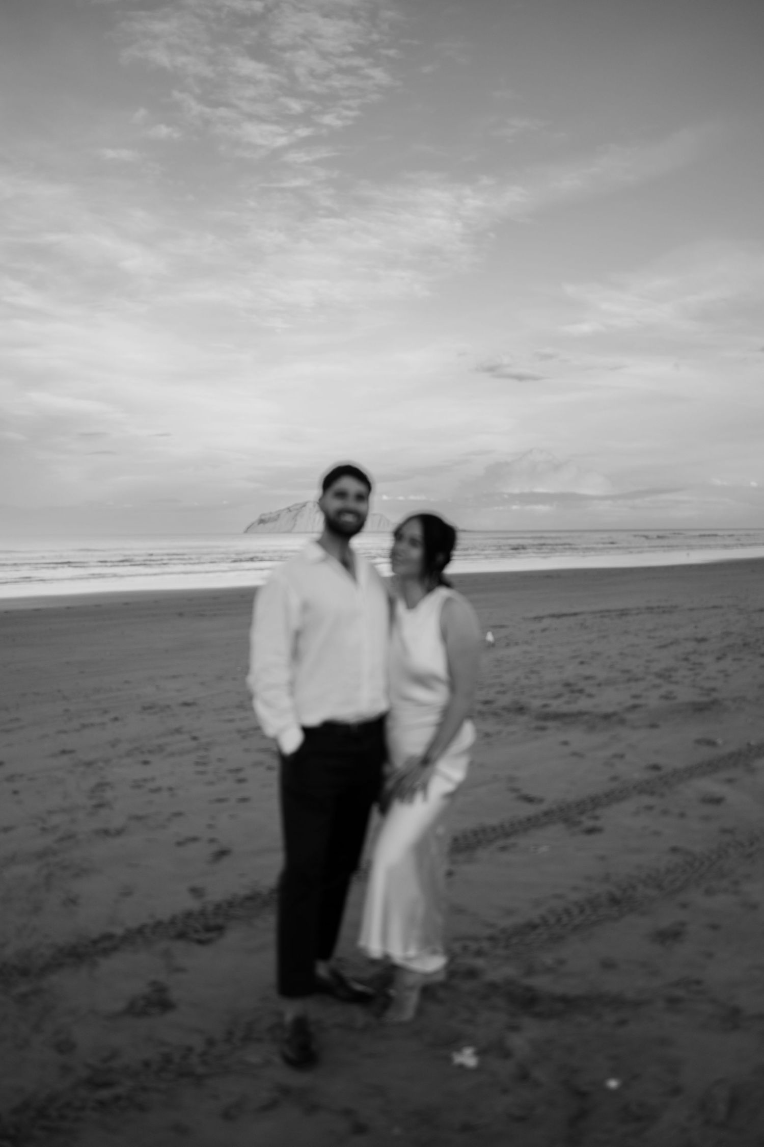 A romantic black and white beach wedding photo with a cloudy sky backdrop.