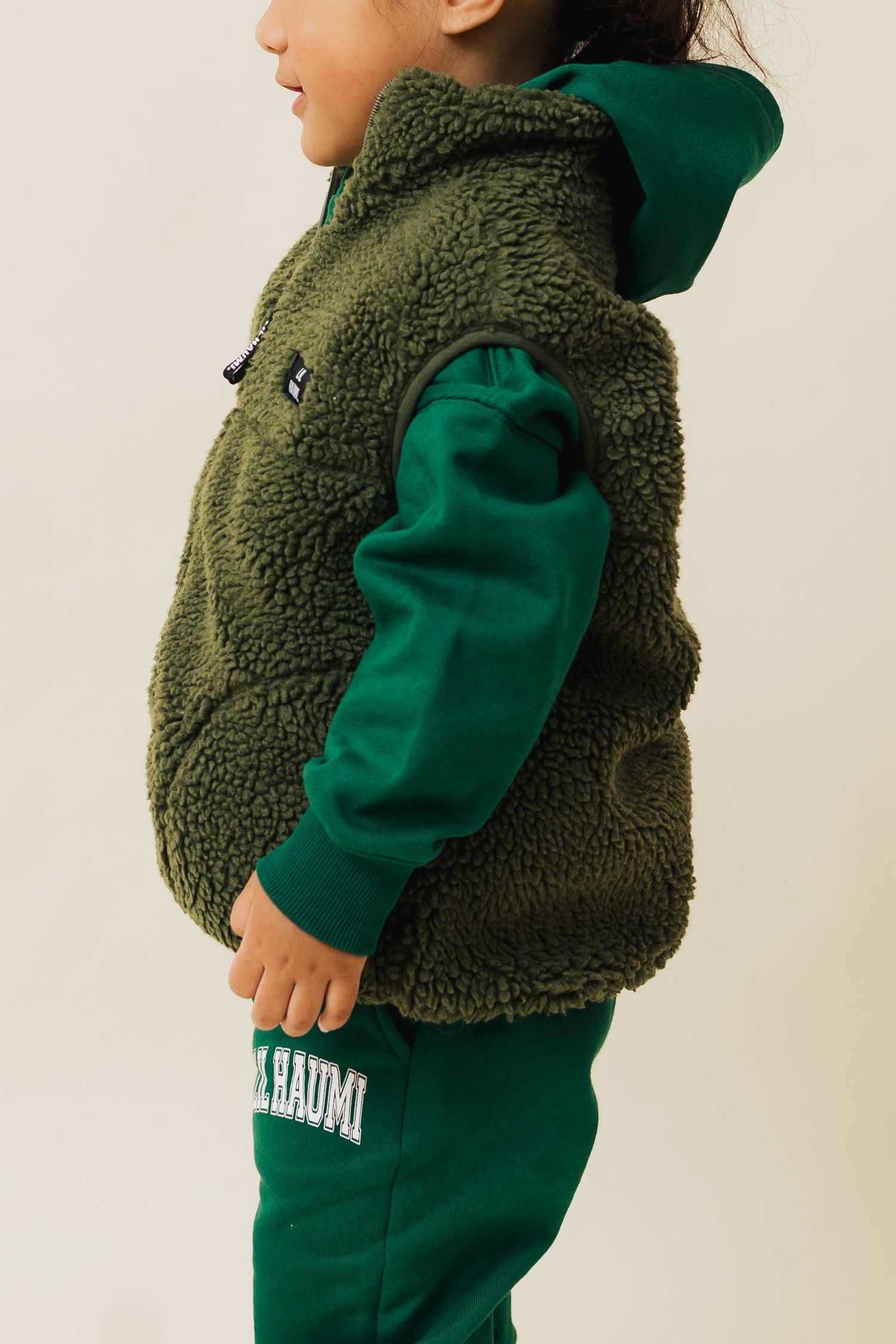 Child wearing a cozy olive sherpa vest over an emerald green sweatsuit in a casual pose.