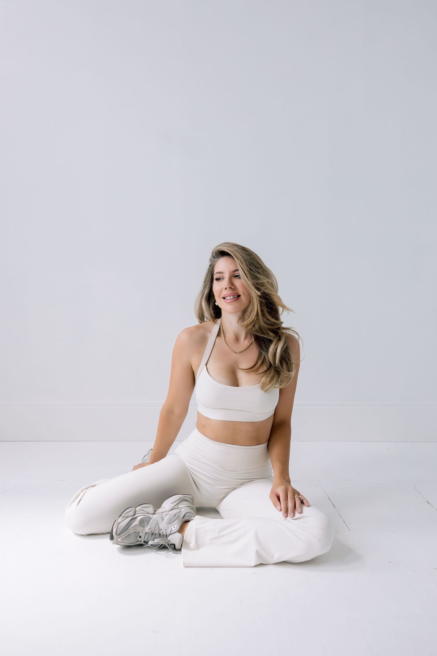 Person in white athletic wear stretches and poses on light background in minimalist fitness photoshoot series.