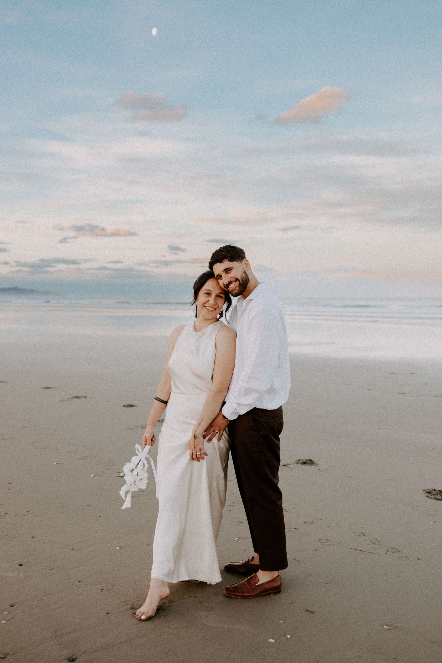 A dreamy sunset beach wedding photo with soft pink clouds and calm ocean waves.