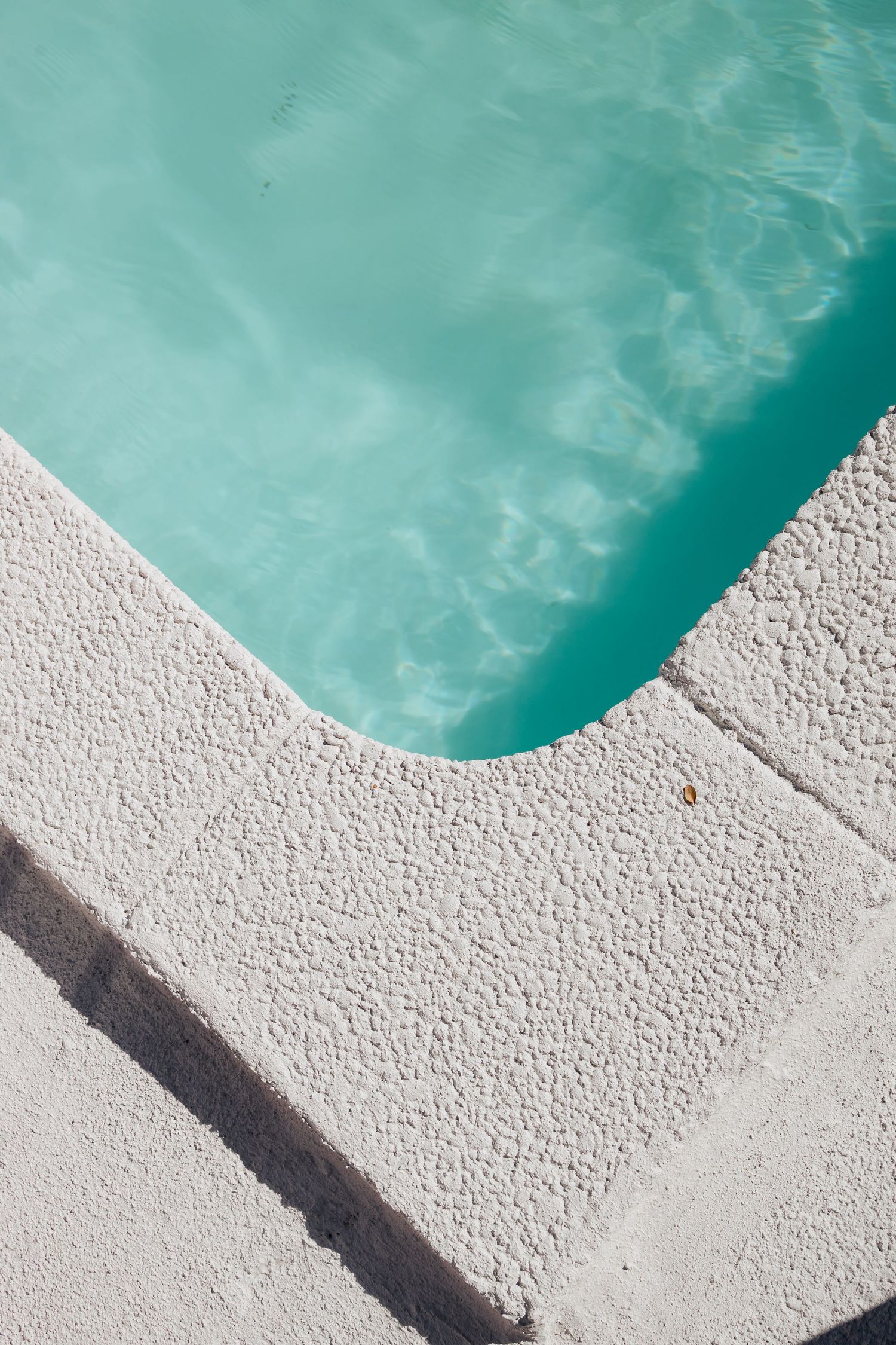 Turquoise pool water meeting white concrete edge in minimalist composition.
