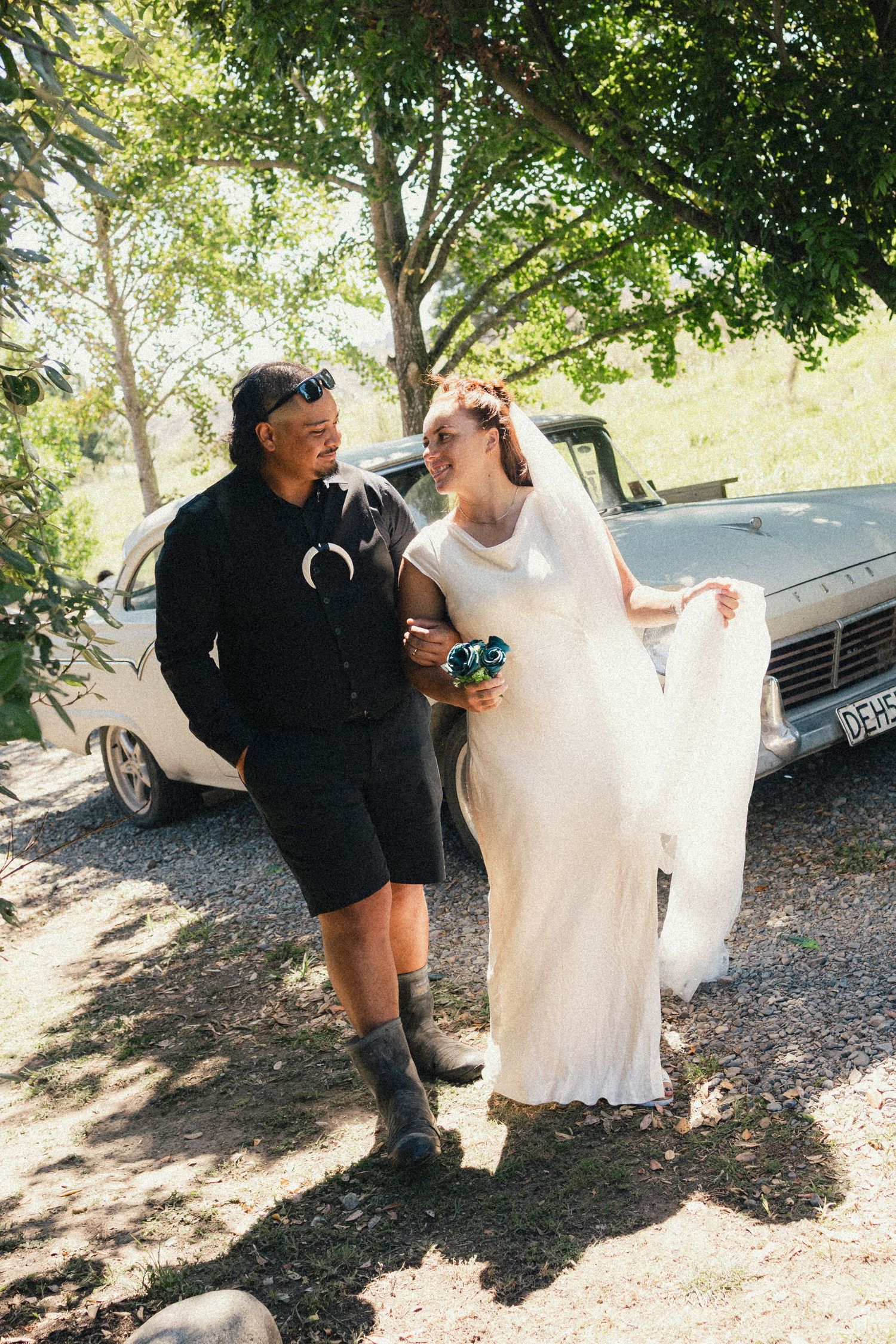 A casual wedding scene outdoors with a vintage car in the background on a sunny day.