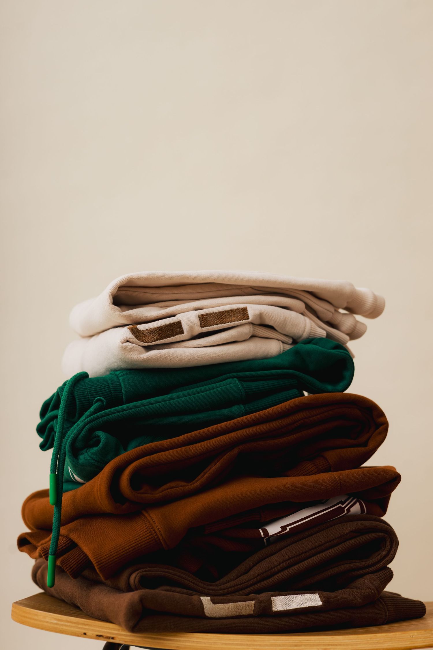 A stack of neatly folded dark brown and green sweaters or garments arranged in a tidy pile on a light surface.
