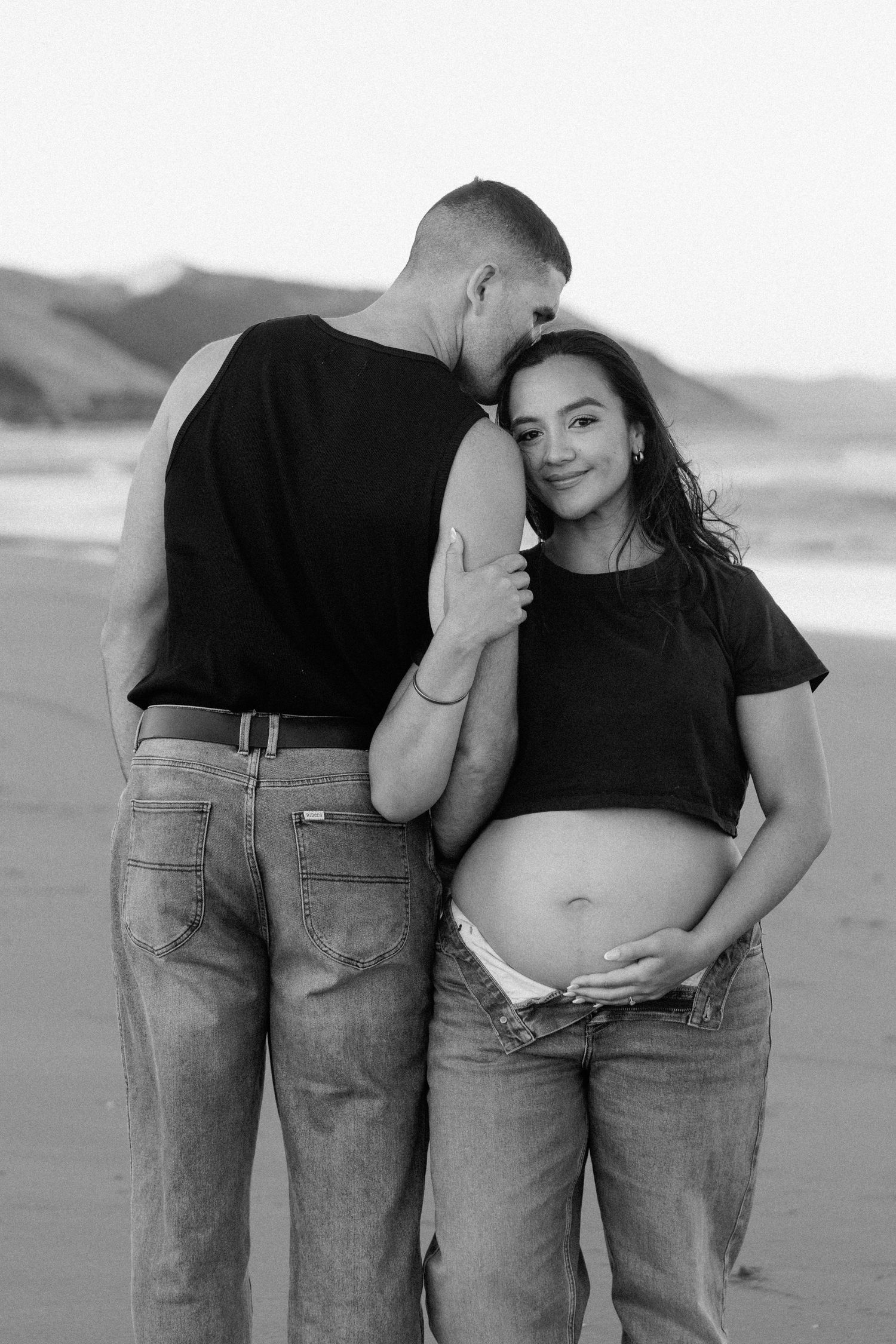 A series of black and white maternity photos showing a couple embracing on a beach.