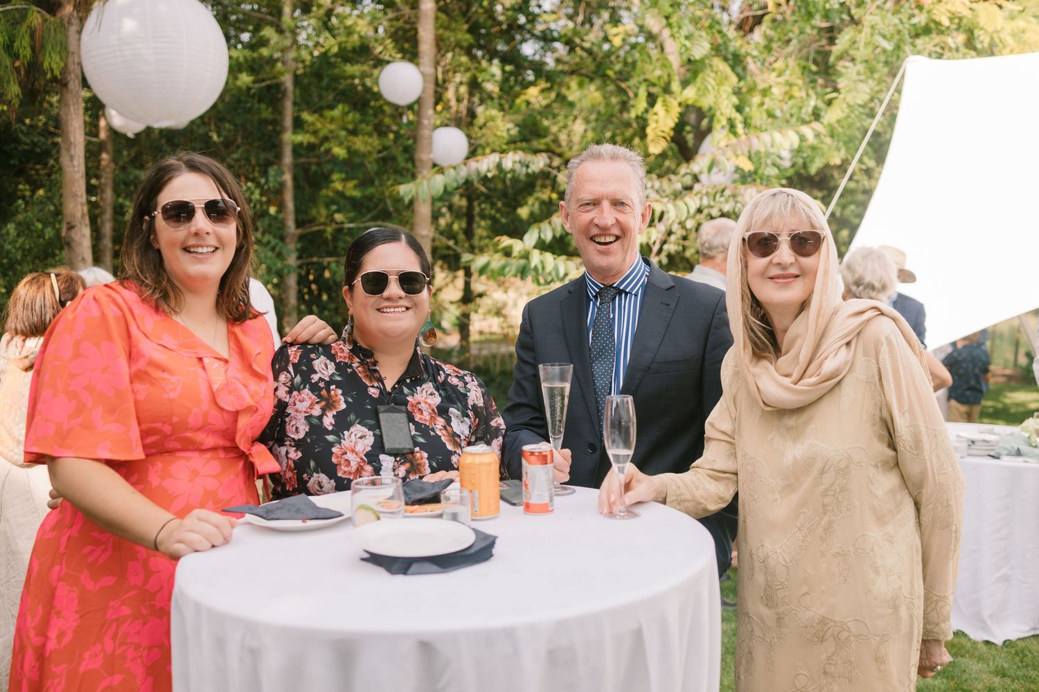 Wedding guests enjoying drinks and conversation at a round table during an outdoor reception.