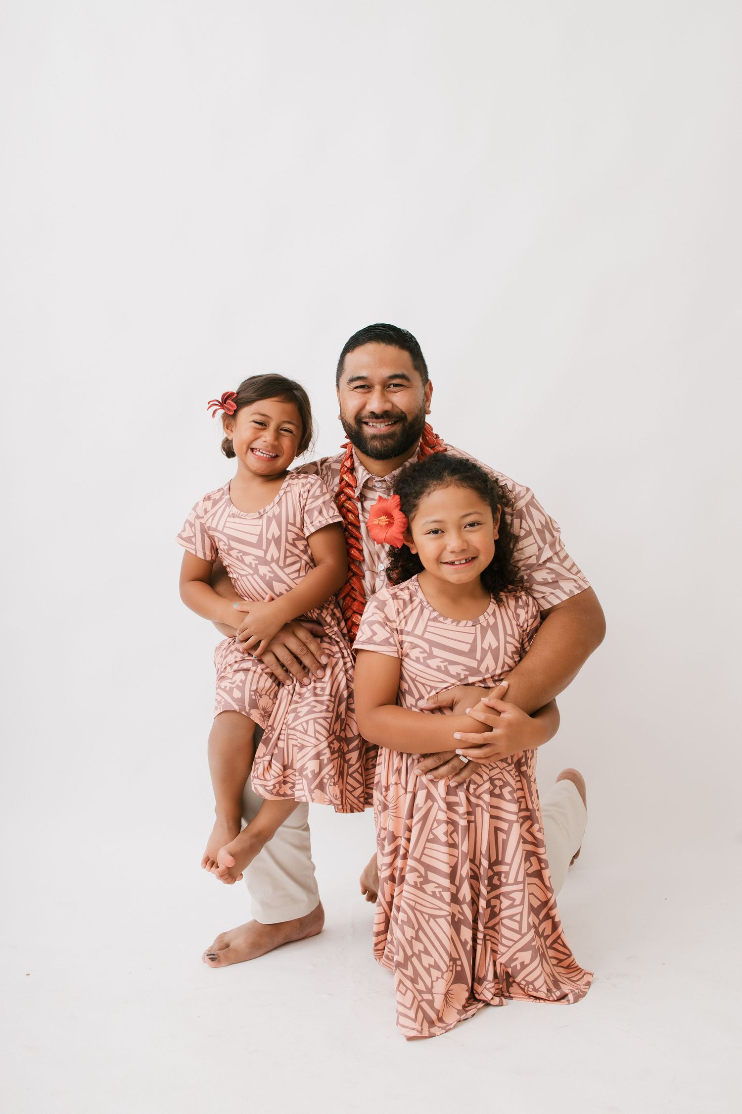 Three people wearing matching pink and white patterned dresses pose together against a white backdrop.